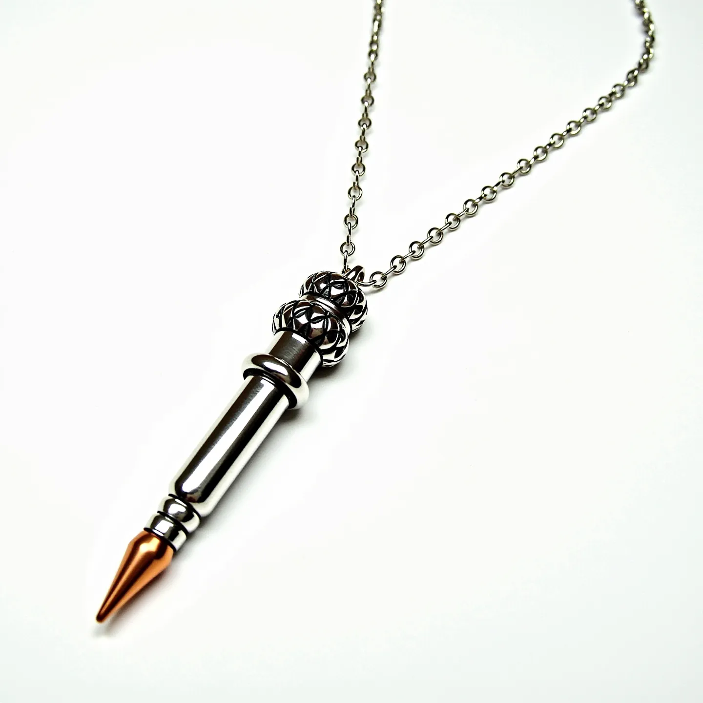 This bullet necklace features a sleek design with a metallic finish, likely made from stainless steel, giving it a modern and durable look. The bullet itself culminates in a copper-colored tip, adding a touch of contrast and elegance. Above the bullet, there is a decorative element which appears to be intricately carved or cast, possibly incorporating a lattice-like pattern. The chain is composed of linked metallic rings, complementing the pendant with its consistent metallic theme. The necklace is fitted with a standard clasp, providing secure attachment and ease of wear.