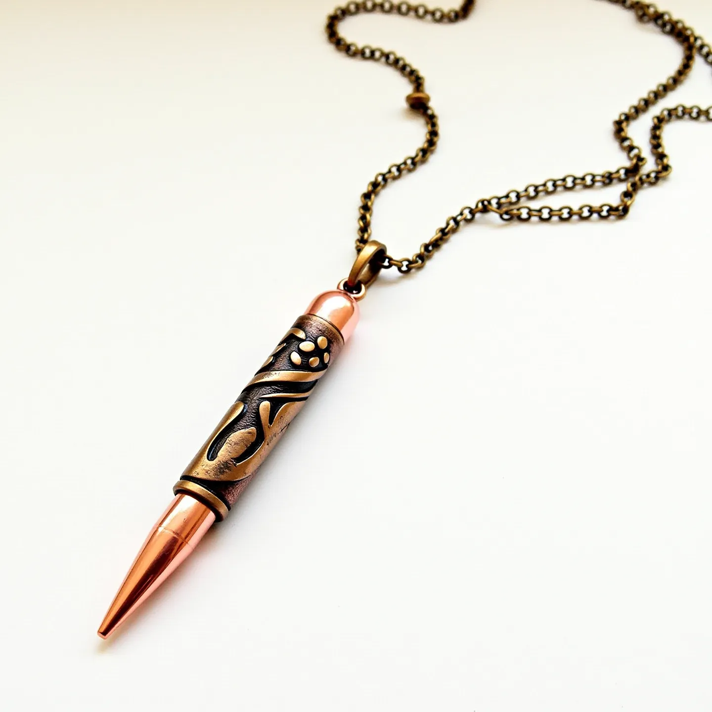 This bullet necklace features a pendant crafted from a polished copper casing that seamlessly tapers into a bullet shape. The pendant is adorned with intricate brass-colored embellishments that include swirling patterns and small metallic accents, adding a decorative touch to its design. It is suspended from an antique-style brass chain, which is attached to the pendant through a robust cap-like loop at the top. The combination of copper and brass elements gives the necklace a vintage and artistic appearance. The necklace closes with a standard lobster clasp, ensuring a secure fit when worn.