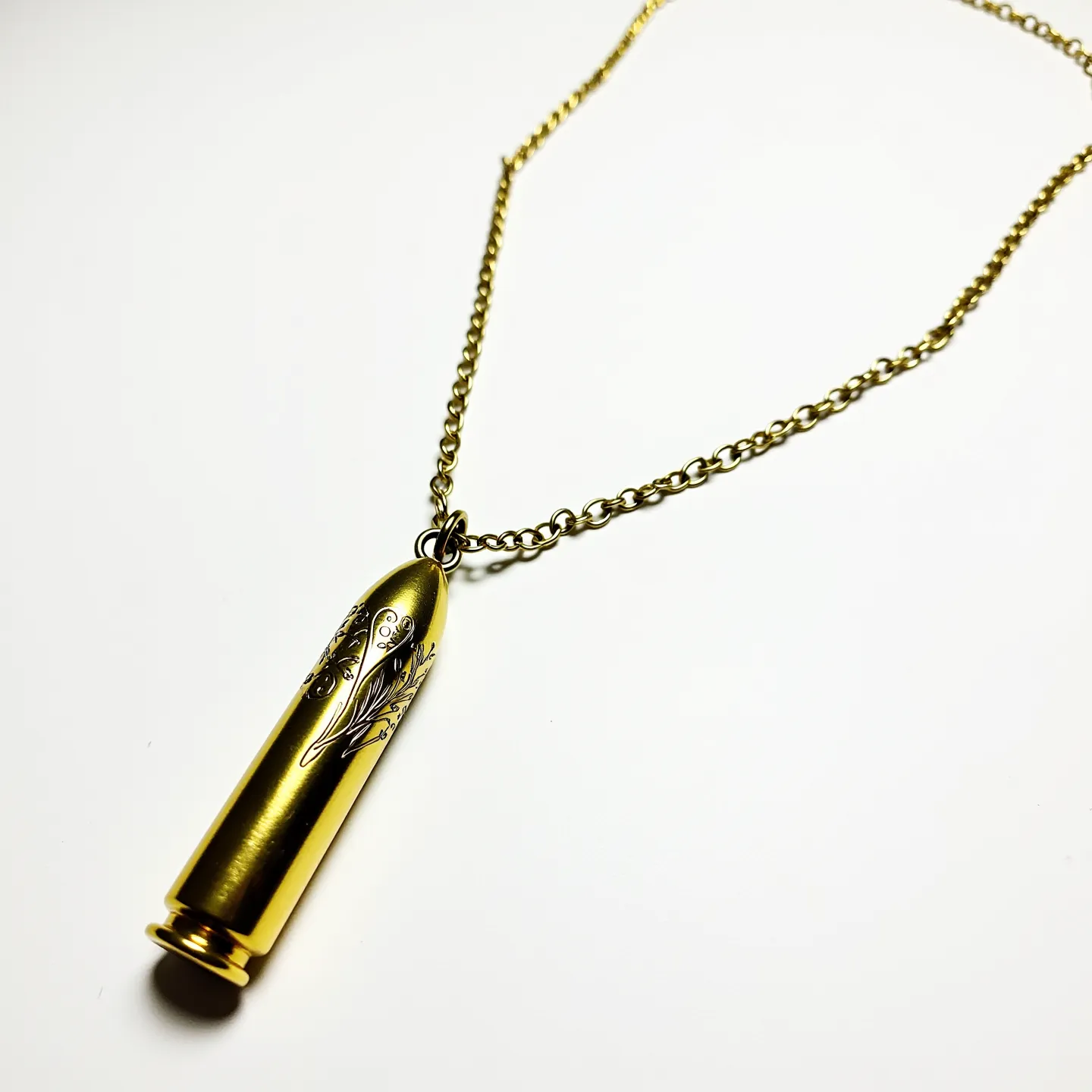 This bullet necklace features a pendant crafted in the shape of a brass-colored bullet, adorned with intricate floral engravings that add an artistic touch to its design. The pendant is attached to a medium-link chain of similar brass or gold-tone material, providing a cohesive look. The necklace is secured with a standard clasp, offering functionality and ease of wear. The absence of any visible gems or stones maintains the focus on the engraved details and the lustrous finish of the metal, making it a striking statement piece.