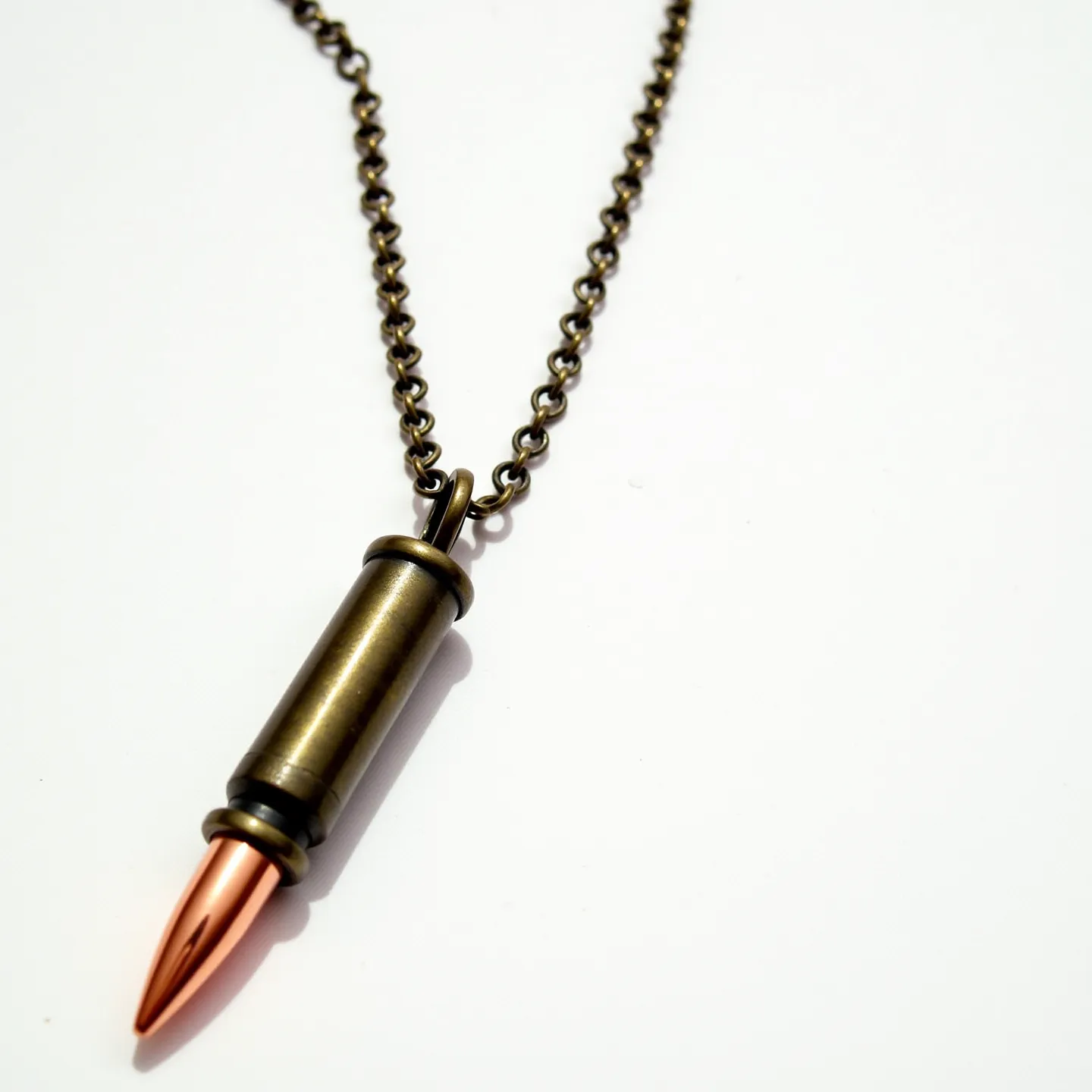 This bullet necklace features a pendant shaped like a bullet, crafted from a metallic material with a polished, dual-toned finish. The casing of the bullet pendant has an antique brass appearance, while the bullet tip itself is a contrasting copper color, enhancing its aesthetic appeal. The pendant is suspended from a fine loop, connecting to a chain of similar antique brass coloration, composed of interlinked circular chain links. The design is simple yet striking, emphasizing the industrial and edgy theme that bullet jewelry often embodies.