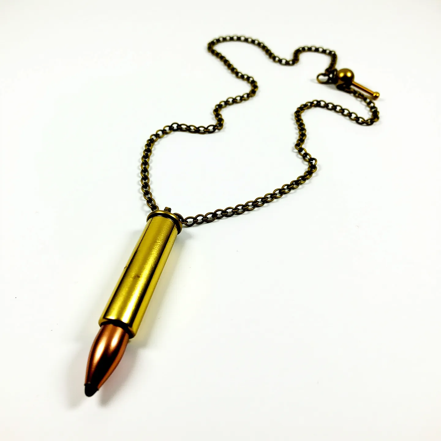 This bullet necklace features a metallic cartridge pendant, showcasing a combination of a brass-colored casing and a copper-tone bullet tip. The pendant is suspended on a classic chain with a rich, antique brass finish, providing a rugged aesthetic. The attachment includes a toggle clasp, which secures the necklace while complementing its overall design with a similar brass hue. The piece is sleek and solid, resonating with a bold and edgy fashion statement.