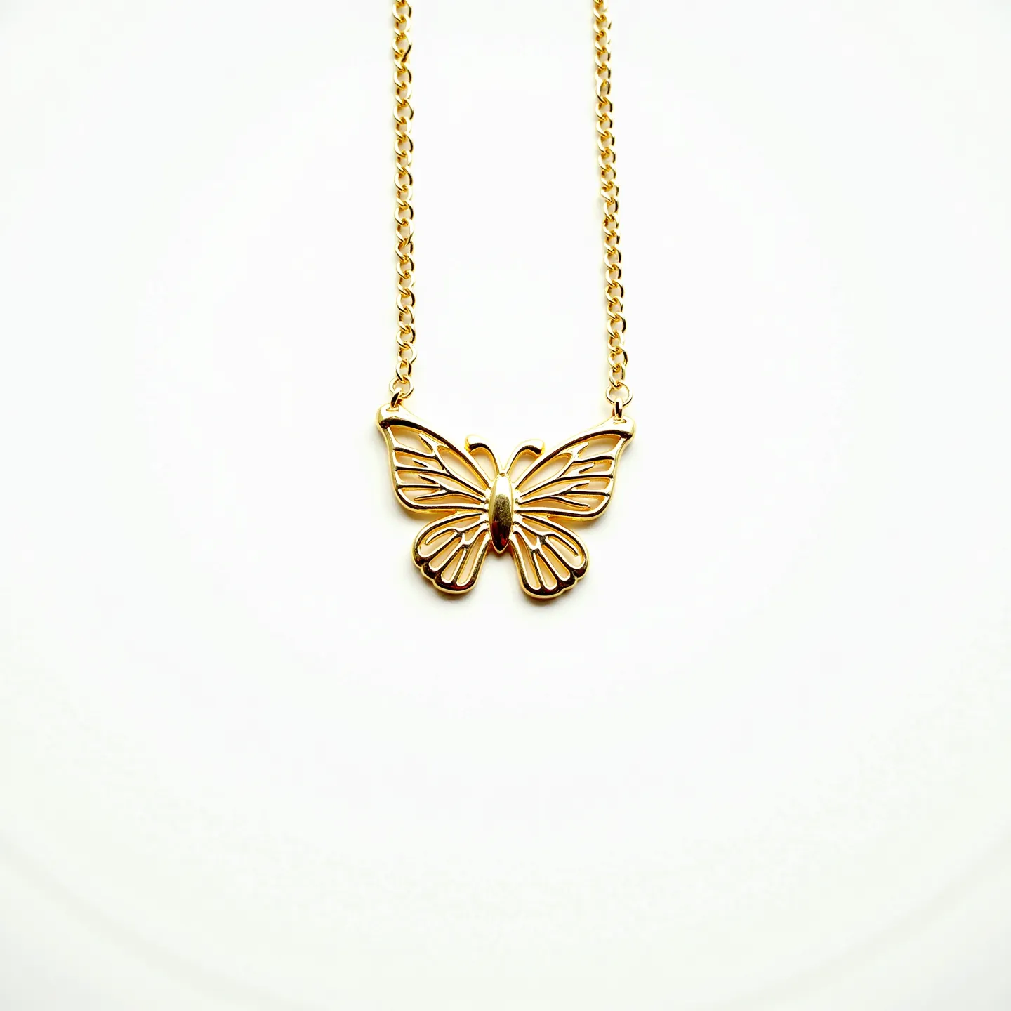 This butterfly necklace showcases a delicate design crafted from gold-toned metal, featuring a gracefully rendered butterfly pendant. The pendant itself displays an openwork style, allowing light to pass through its intricate patterns, thus enhancing its elegant appeal. The central part of the butterfly has a solid metallic body, offering contrast to the otherwise airy design. The necklace is held together by a fine chain that complements the overall aesthetic. The attachment points are subtle, blending seamlessly with the rest of the piece, ensuring a smooth transition between pendant and chain.