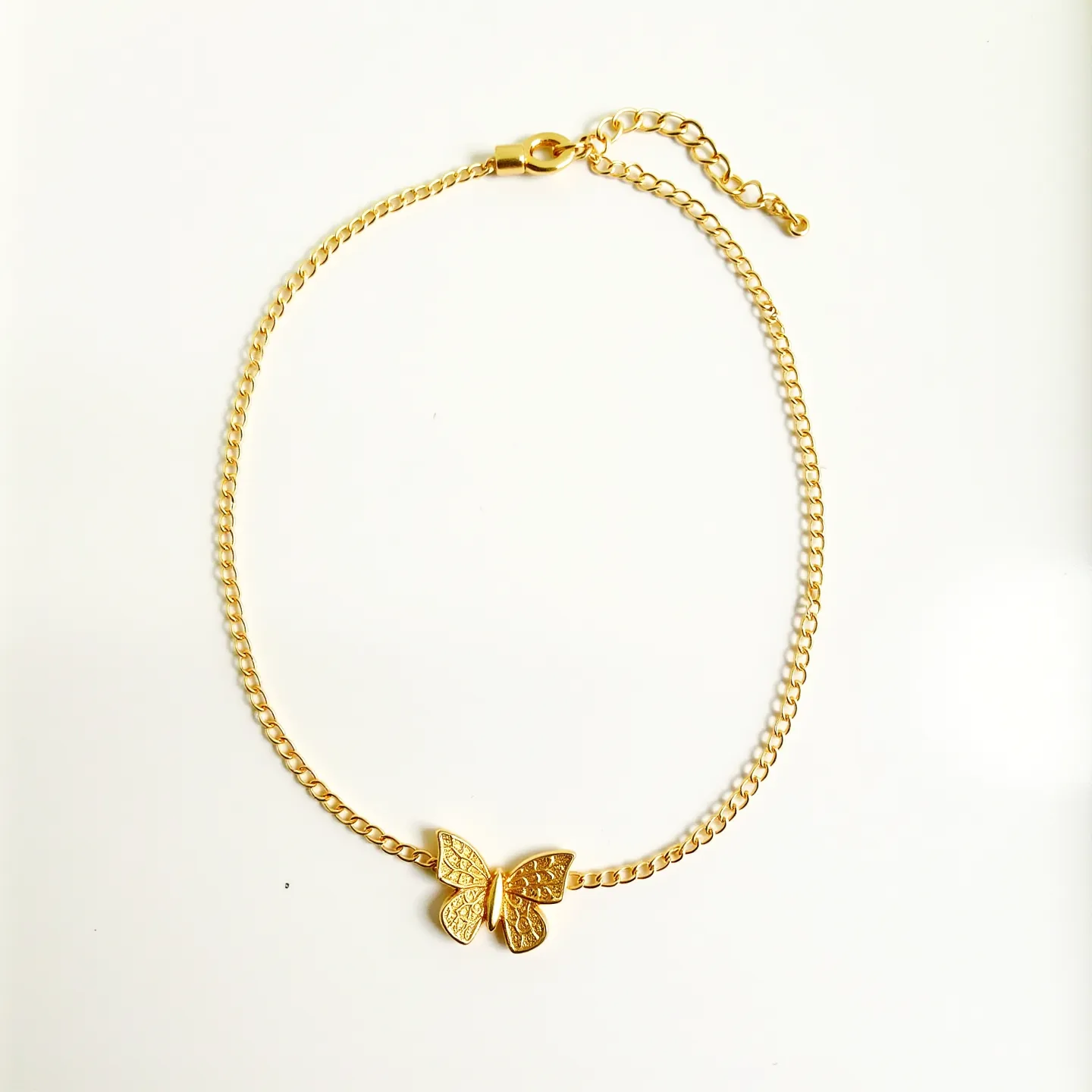 This butterfly necklace features a delicate gold-toned chain with a central butterfly motif that adds a whimsical touch. The butterfly is crafted from a similar gold-toned material, with intricate detailing on the wings, reminiscent of filigree work, providing a textured appearance. This piece is further enhanced by the use of a lobster clasp, which offers a secure and adjustable fit through an extension chain, making it versatile for various neck sizes. The necklace beautifully combines elegance and playfulness, perfect for both everyday wear and special occasions.