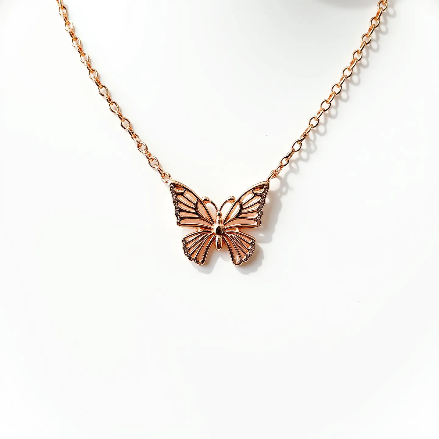 This butterfly necklace features a delicate pendant crafted in rose gold-toned metal, showcasing an intricately designed butterfly with defined wings and a smooth body. The wings are accented with tiny, round, clear stones that add a touch of sparkle to the piece. The pendant is suspended from a fine rose gold-toned chain, which enhances its elegant appearance. The butterfly is connected to the chain at two points, ensuring it hangs evenly. The necklace likely has a standard clasp mechanism for secure attachment when worn.