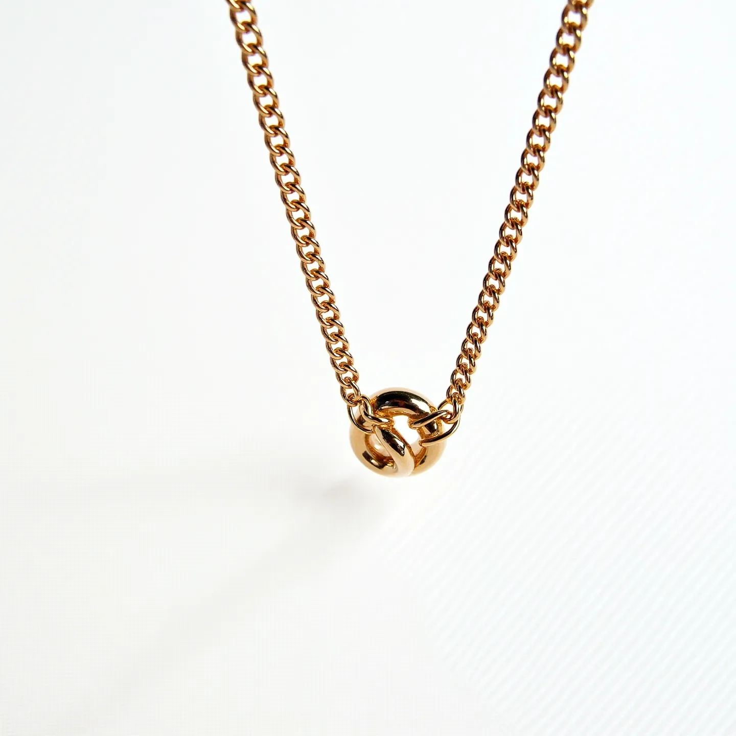 This cable chain features a lustrous gold-tone material, suggesting a polished metal construction, which enhances its elegance and classic appeal. At the center, a small, round charm is integrated into the design, adding visual interest with its smooth, reflective surface. The charm does not appear to include gems or stones, focusing instead on the sleek, minimalistic aesthetic of the metal itself. This chain is likely secured with a standard clasp, common in chain necklaces, ensuring it is both functional and stylish.