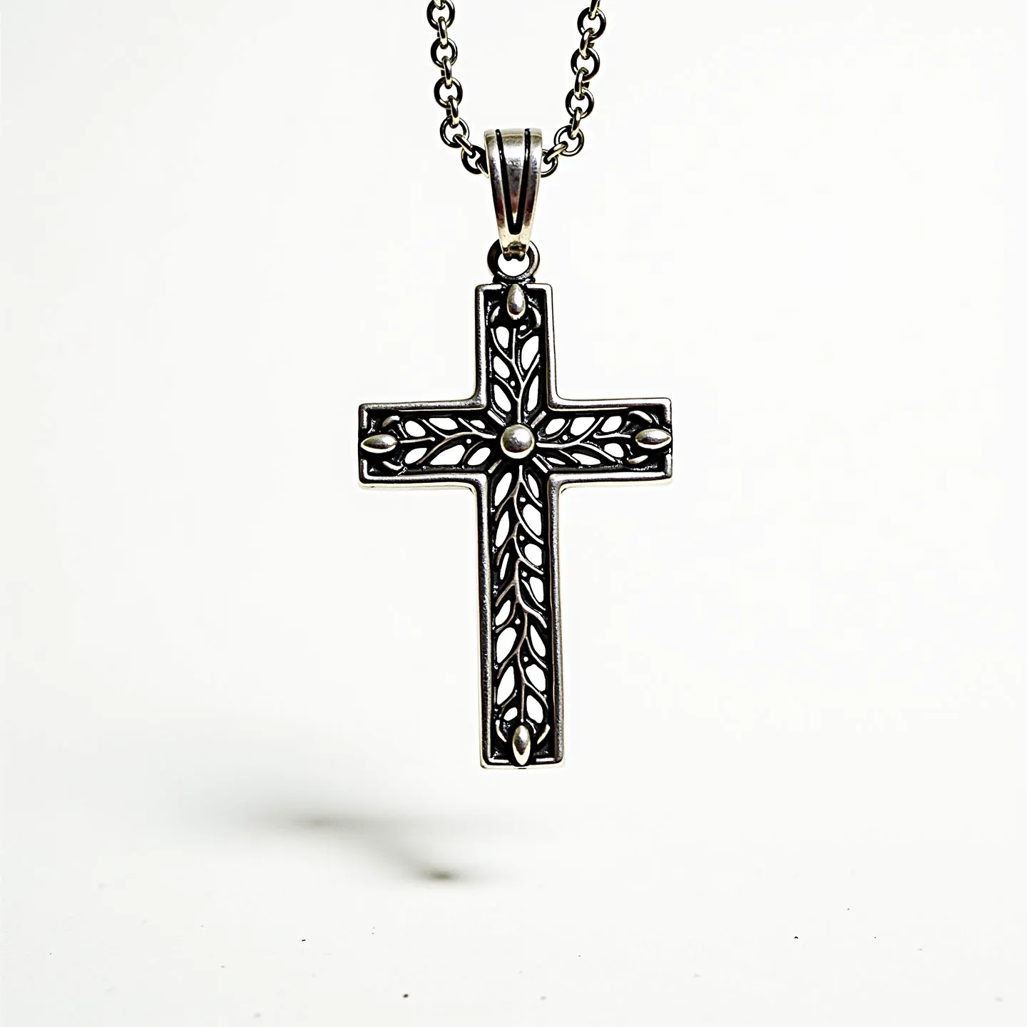 This catholic cross necklace features an intricate design made from metal, likely silver or a silver-toned alloy, showcasing an ornate pattern of leaves and openings that add depth and texture. At the center and tips of the cross are small, rounded metal accents that give the piece a refined elegance. The cross hangs from a complementary chain with interlocking links, offering a sturdy yet stylish appearance. The attachment includes a classic bail that allows the cross to dangle freely from the chain, ensuring it lays flat when worn.