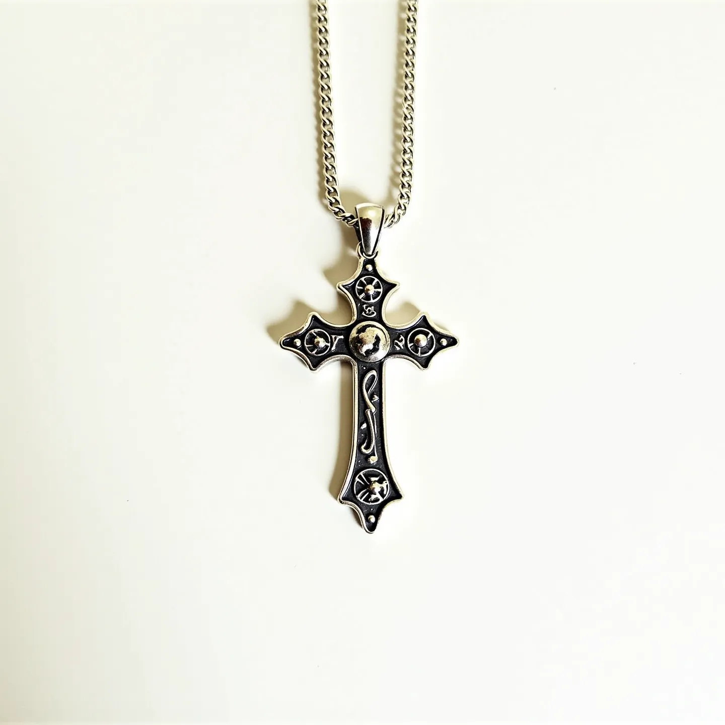 This Catholic cross necklace features an intricately designed pendant crafted from what appears to be a polished silver material. The cross showcases ornate detailing and includes small, round gemstones set within each of the four cross points, possibly serving an aesthetic purpose with dark accents that enhance their visibility. The stones are well-faceted, adding a subtle sparkle to the piece, and are likely secured in a prong or bezel setting, ensuring durability. The necklace is attached to a textured chain, likely made of the same silver material, which complements the pendant. Its secure connection is facilitated by a sleek bail that allows for easy movement along the chain.