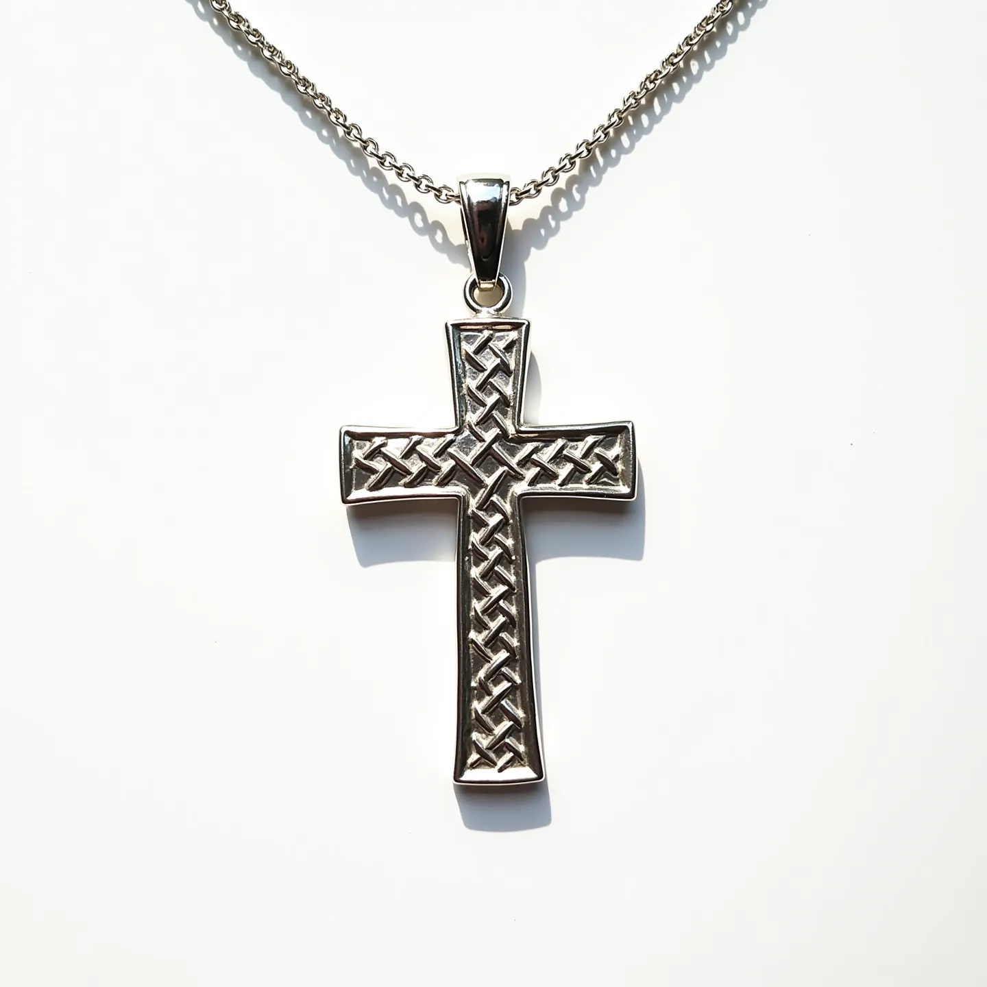 This catholic cross necklace features a striking metallic design, crafted from a polished silver-toned material. The cross itself is intricately detailed with a woven pattern, creating an elegant and textured appearance. The pendant is suspended from a sturdy, silver-toned chain that enhances its sophisticated look. At the top, the cross connects to the chain with a smooth and shiny bail, providing a seamless transition. The chain is designed with a classic link style, contributing to the necklace's overall durability and timeless appeal.