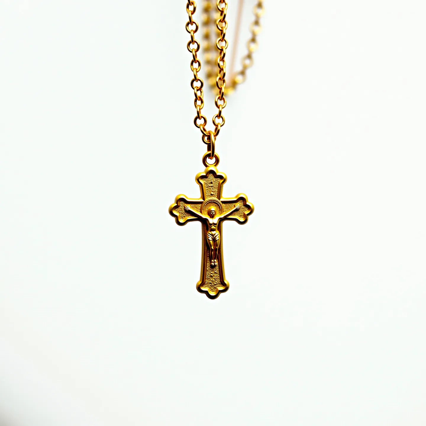 This Catholic necklace features a gold-toned metal cross pendant intricately designed with religious iconography, including a depiction of a figure that appears to represent Jesus Christ. The cross exhibits a detailed and raised relief pattern, giving it a textured surface that enhances its visual appeal. The pendant is suspended from a matching gold-toned chain composed of uniform, oval links, which provide a sturdy yet elegant structure. The necklace appears to be equipped with a standard clasp, ensuring secure fastening when worn. Overall, the craftsmanship highlights both devotion and artistry in its design.