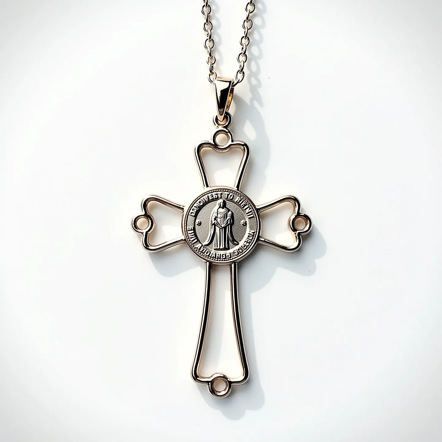 This Catholic necklace features an intricate open-design cross crafted from a shiny metal, likely silver or gold-plated, with a central medallion. The medallion is intricately embossed with an image of a saint encircled by a border of text. The pendant is attached to a delicate link chain via a simple yet sturdy bail. The chain, composed of interlocking metallic loops, complements the pendant’s design, enhancing the overall elegant and spiritual appearance of the piece.