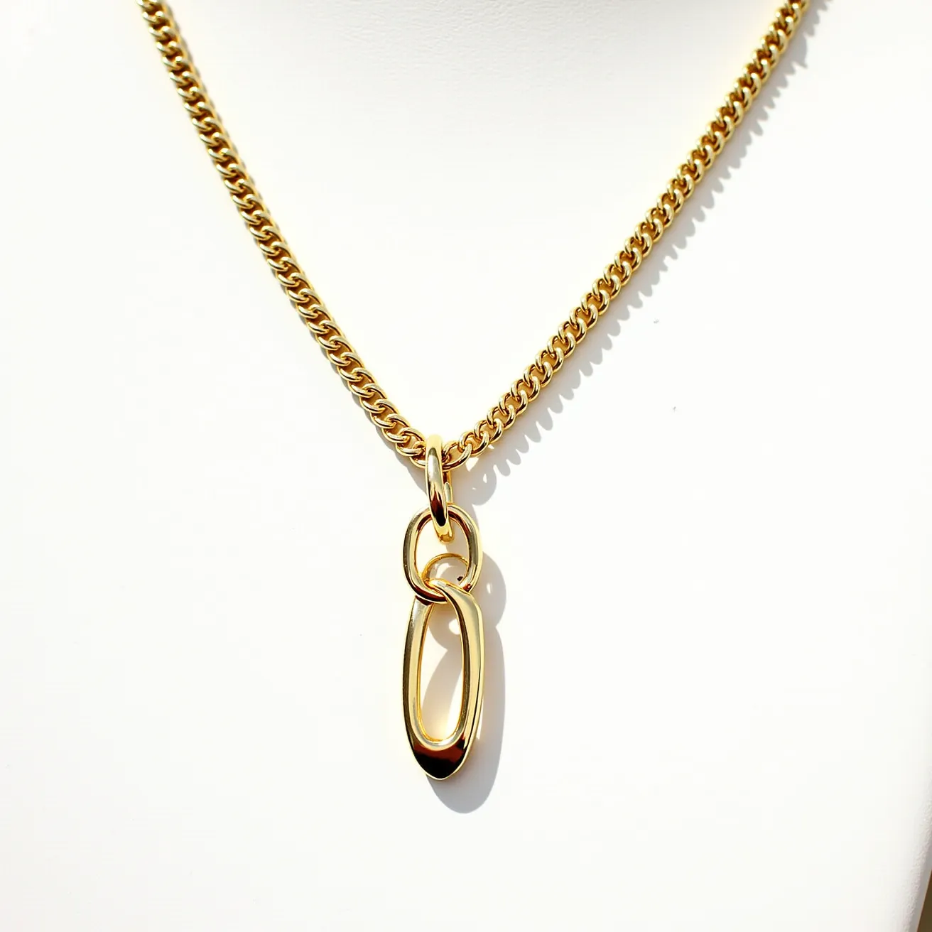 This chain link necklace features a polished gold-tone finish, adding a luxurious and elegant appearance. The necklace includes a series of interlocking chain links, designed with a smooth, uniform pattern. Hanging from the center is a unique elongated oval pendant, creating a focal point that enhances its overall design. The pendant connects seamlessly with the necklace through smaller circular links, maintaining a cohesive aesthetic. The clasp is designed for secure wear, blending discreetly into the design to maintain the necklace's sleek and continuous look. The craftsmanship reflects both style and sophistication, making it a versatile accessory.