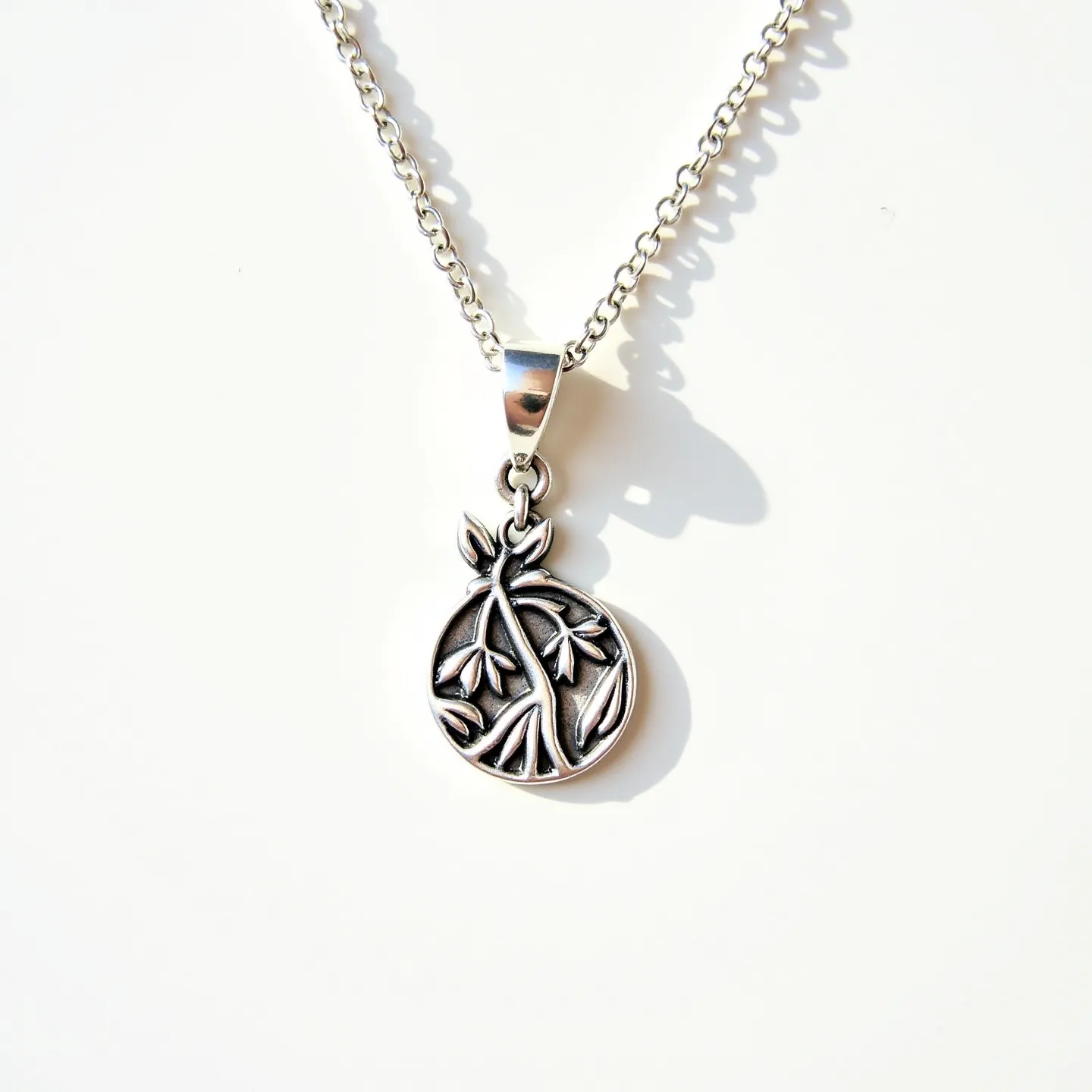 This charm necklace features a round pendant with an intricate design of leaves and branches, crafted from what appears to be a silver metal. The pendant is suspended from a matching silver chain, which is composed of closely linked, smooth oval links that give it a sturdy yet elegant appearance. The necklace is finished with a simple yet secure lobster clasp, ensuring ease of wear and removal. No gemstones or additional embellishments are present, allowing the detailed craftsmanship of the pendant to be the focal point of the piece.