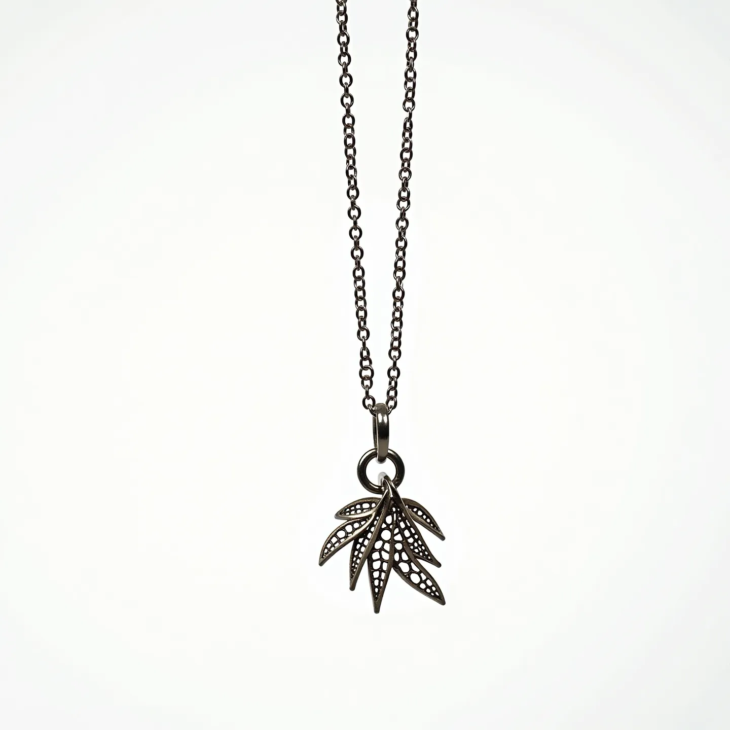 This charm necklace features a dark metal chain with an intricate pendant composed of multiple leaf-like charms. The charms have a delicate, filigree design with perforations, suggesting careful craftsmanship and artistry. The pendant is suspended from a circular loop that is securely attached to the chain. The overall aesthetic is both modern and nature-inspired, with a focus on detailed metalwork. The necklace is equipped with a standard metal clasp to ensure ease of wear and security.