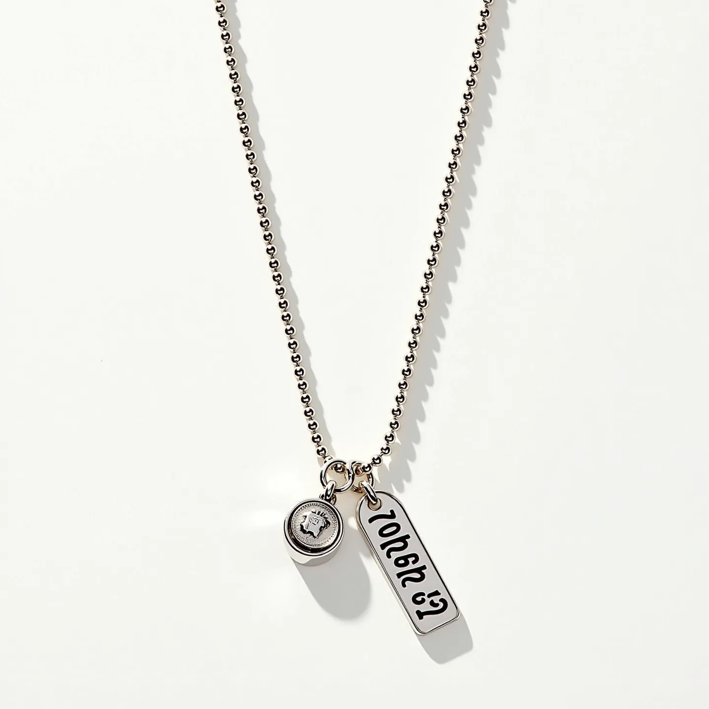 This charm necklace chain features a delicate ball chain made from a silvery metal, likely stainless steel or a similar alloy, providing both strength and elegance. The chain supports two distinct charms: one is a circular charm housing a round-cut stone, set in a sleek bezel that showcases its brilliance, which suggests it could be a crystal or a cubic zirconia. The second charm is a rectangular metal tag with engraved characters, adding a personalized element to the design. The necklace is equipped with a standard clasp, ensuring secure and easy wearability.