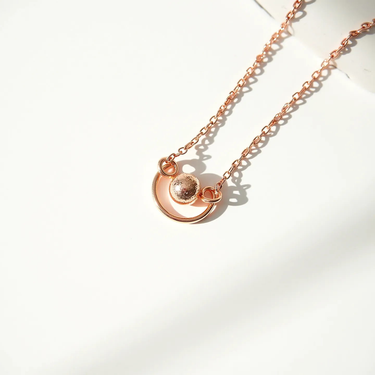 This charm necklace chain features a delicate design crafted from a rose gold-toned material, providing a warm and elegant appearance. The central charm includes a small, spherical element that exhibits a textured finish, creating an eye-catching focal point. The chain links are simple yet refined, complementing the charm without overpowering it. The charm is attached to the chain through small loop connectors, adding to the cohesive design. There is no visible clasp or attachment shown in the image, suggesting a continuous loop design.