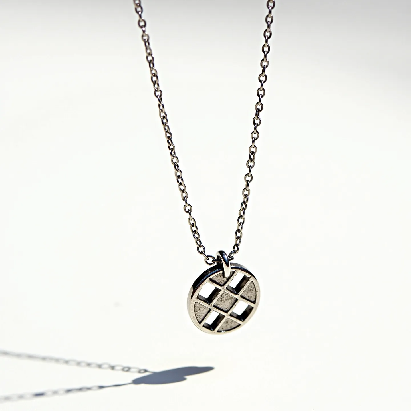 This charm necklace chain is crafted from a sleek metal, likely silver or white gold, with a simple and elegant link chain design. The charm itself is a circular pendant featuring a geometric pattern with a grid-like design, giving it a modern and minimalist aesthetic. The charm is attached to the chain using a small loop, ensuring it hangs securely. The chain appears to have a classic clasp mechanism for fastening, providing ease of wear. The overall design is contemporary, with a focus on clean lines and subtle sophistication.