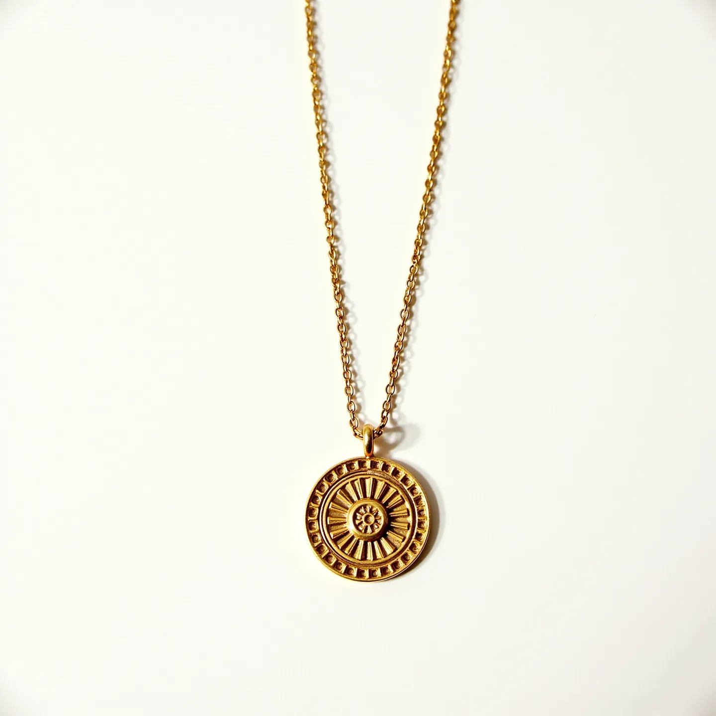 This charm necklace chain features a gold-toned metal finish with an intricately designed circular pendant. The pendant displays a pattern reminiscent of a sunburst, with its center detailed with a floral-like motif surrounded by radial lines and bordered accents. The chain appears to be a fine link style, which complements the size and aesthetic of the pendant. At the top of the charm, there's a small loop that attaches to the chain, allowing for easy movement and highlighting the pendant as the focal point. The clasp is not visible, but commonly in such designs, it could be a spring ring or lobster clasp for secure fastening.