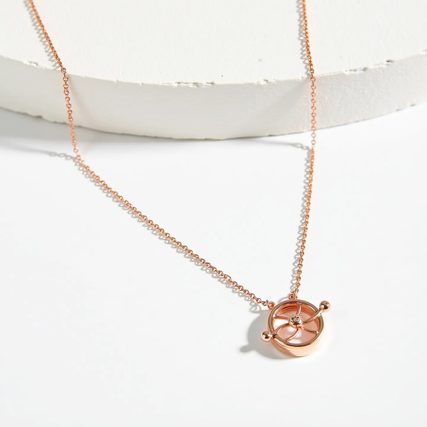 This charm necklace chain is crafted from a delicate rose gold metal, featuring a striking circular pendant reminiscent of a ship's wheel. The pendant is accented with a small, round-cut diamond, centrally set to catch the light beautifully. The piece is elegantly linked with a fine, matching cable chain which ensures a seamless design. The necklace appears to be secured with a sturdy, coordinating clasp that complements the overall elegance and intricacy of the design.