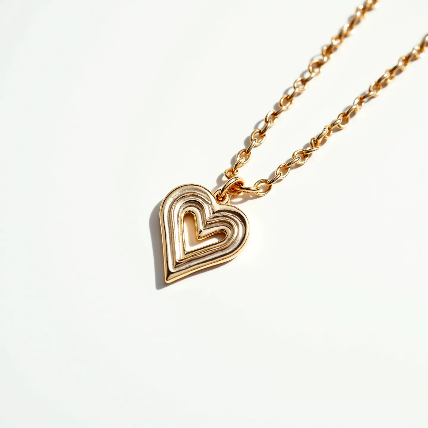 This charm necklace chain features a beautifully designed heart-shaped pendant. The pendant showcases a layered, open-heart design, crafted from a shiny gold-tone metal. Its chain is composed of interlocking links that reflect the same golden hue, adding to the cohesive and elegant appearance of the piece. The attachment holding the pendant to the chain is a simple, yet secure loop, which allows the charm to hang gracefully. Overall, the necklace exudes a timeless and classic look, suitable for both everyday wear and special occasions.