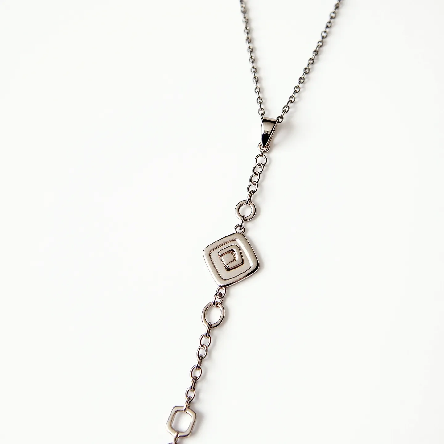 This charm necklace chain features a delicate metallic composition with a sleek, polished appearance. The chain is linked with small, uniformly sized rings that create a consistent, flowing design. At the center of the necklace, there is a geometric charm with interlinked square shapes, adding a modern and minimalist touch. The necklace is fitted with a sturdy, well-integrated clasp that ensures secure fastening and ease of wear. The overall design exhibits a contemporary elegance, suitable for various occasions.