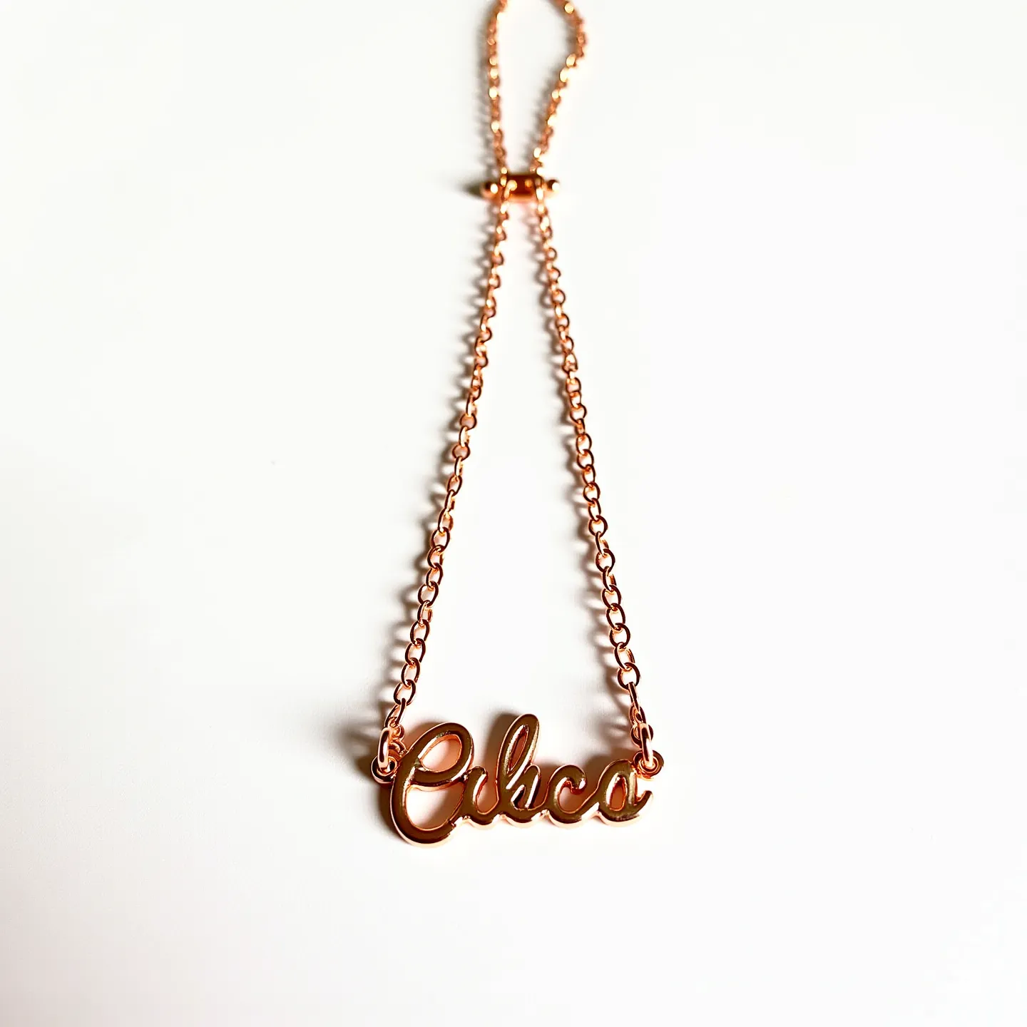 This charm necklace chain features a delicate design crafted from a rose gold-colored metal, giving it an elegant and modern appeal. The chain consists of interlinked oval links, supporting a charm that spells out "chico" in a cursive script that matches the chain's metallic hue. The letters are smoothly polished, contributing to the necklace's cohesive and refined aesthetic. A simple, small jump ring connects the charm to the chain on each side, ensuring stability and fluidity in movement. The necklace is secured with a cylindrical toggle clasp, offering ease of use while maintaining the overall sophisticated look.