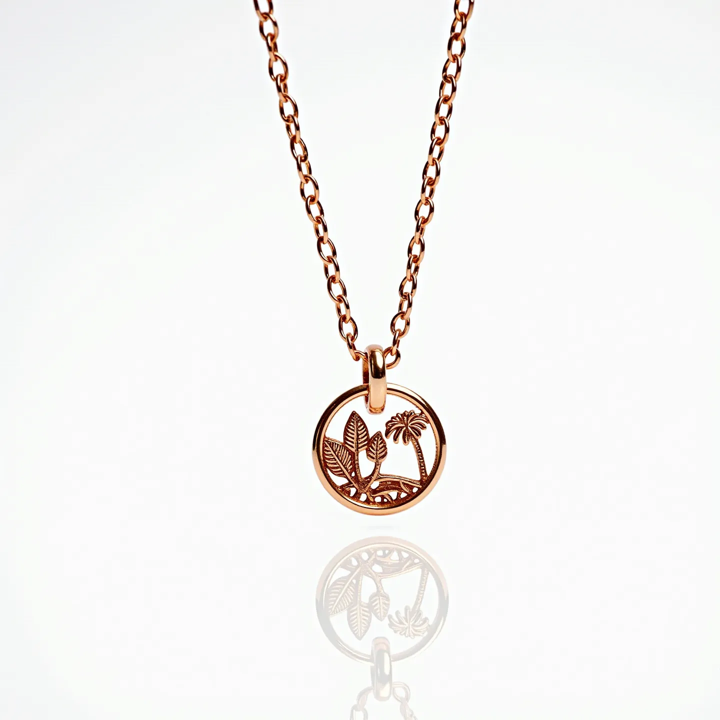 This charm necklace gold features a delicate chain with a round pendant. The pendant is crafted in gold, showcasing an intricate design of leaves and a palm tree within a circular frame. The chain links are uniform and elegantly support the pendant. The clasp is not visible in the image, but the necklace appears to hang smoothly, indicative of a likely secure attachment at the back. The overall design emphasizes simplicity and elegance, with a focus on the natural motifs engraved on the pendant.