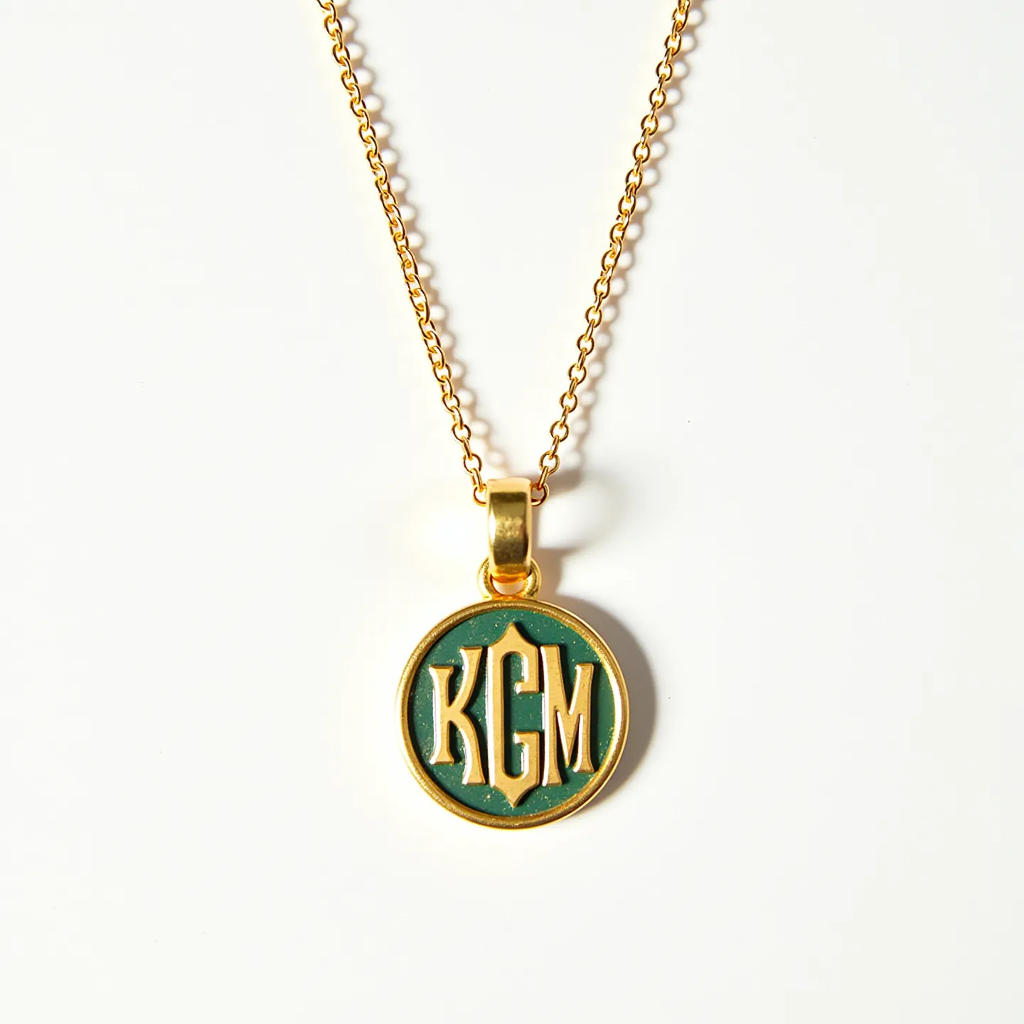 This charm necklace gold features a round pendant with a monogram design reading "KGM" set against a green background. The pendant is crafted from a polished gold material, complementing the intricate detailing of the letters. It hangs from a delicate gold chain, showcasing a simple yet elegant design. The attachment includes a small gold loop connecting the pendant to the necklace, and the chain likely features a standard clasp for secure fastening. There are no visible gemstones embedded in the necklace or pendant.