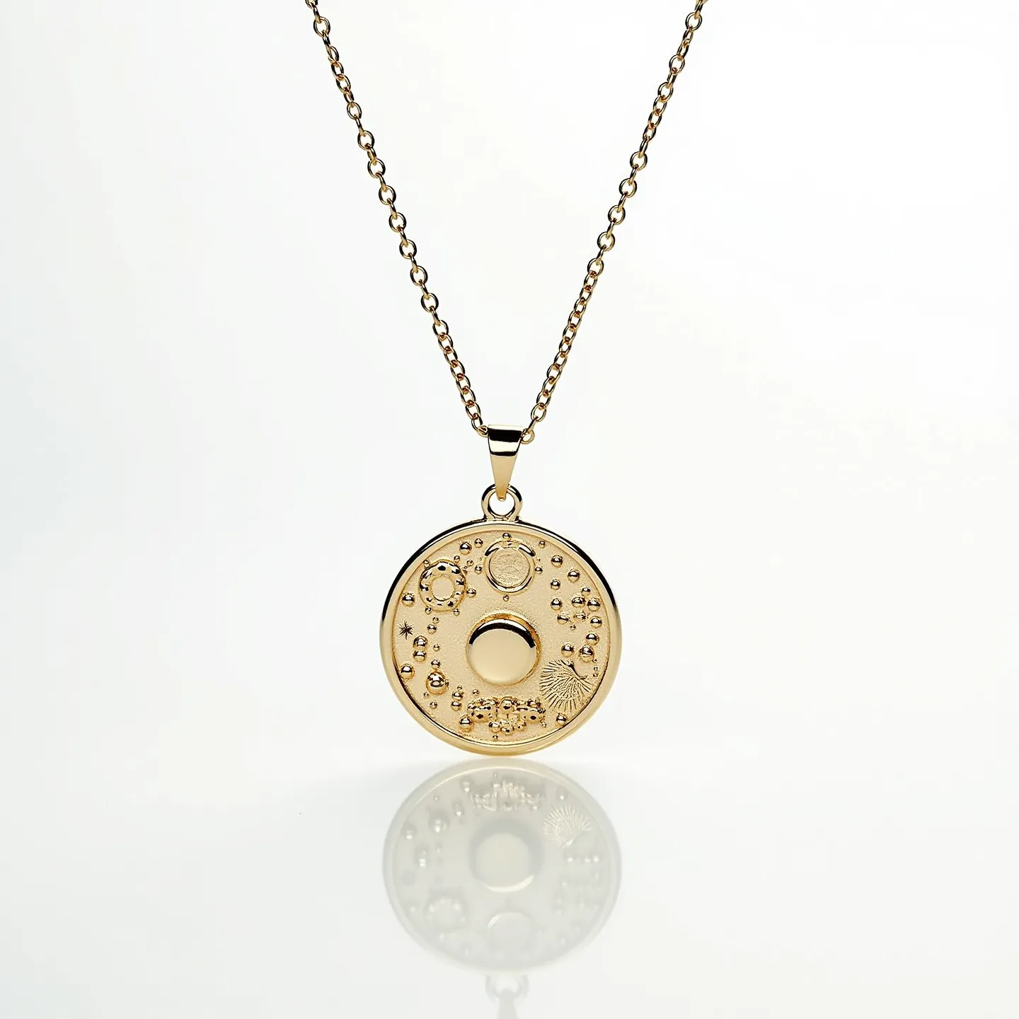 This charm necklace gold features a delicate chain with a lustrous round pendant crafted from gold. The pendant showcases intricate celestial patterns including small raised circles and star-like designs. These details create a textured effect, capturing light beautifully. The pendant is attached with a small, gold loop that connects seamlessly to the chain. The chain itself is fashioned in a classic cable style, offering a secure yet elegant support for the pendant. While the necklace does not feature visible gemstones, the detailed designs on the pendant add visual interest and sophistication.