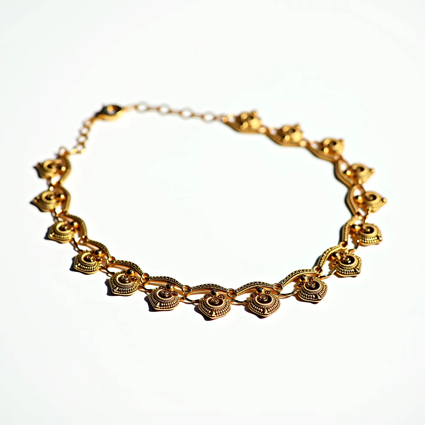 This choker chain features an intricate design with recurring ornate motifs resembling floral or spiral patterns. Made of gold-toned metal, the chain links are elegantly crafted, suggesting a high level of artisanal detail. Each motif is carefully linked to the next, creating a symmetrical and harmonious appearance. The choker includes a small chain extension that allows for adjustable sizing, and it is secured with a classic lobster clasp, ensuring ease of use while enhancing its overall aesthetic appeal. The absence of large gemstones highlights the metalwork's unique design elements.