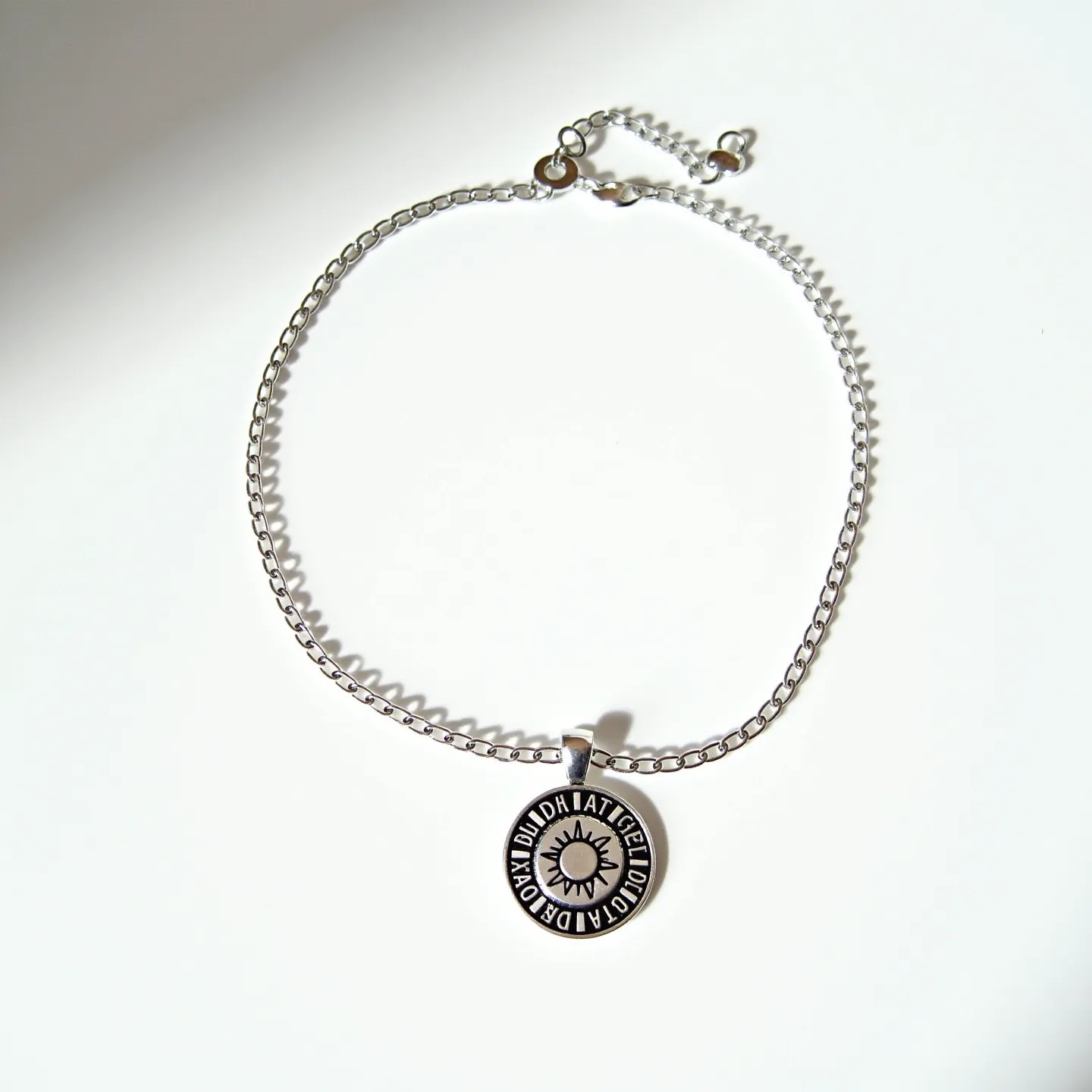 This choker chain features a simple, elegant design made from what appears to be a silver-toned metal, suggesting it could be either sterling silver or a high-polish stainless steel. The chain holds a round pendant with an engraved design, featuring a sunburst pattern encircled by text. The pendant hangs from the center, adding a focal point to the choker. The chain is equipped with an adjustable clasp, providing flexibility in length and ensuring a secure fit around the neck. The craftsmanship suggests both durability and style, suitable for casual or semi-formal wear.