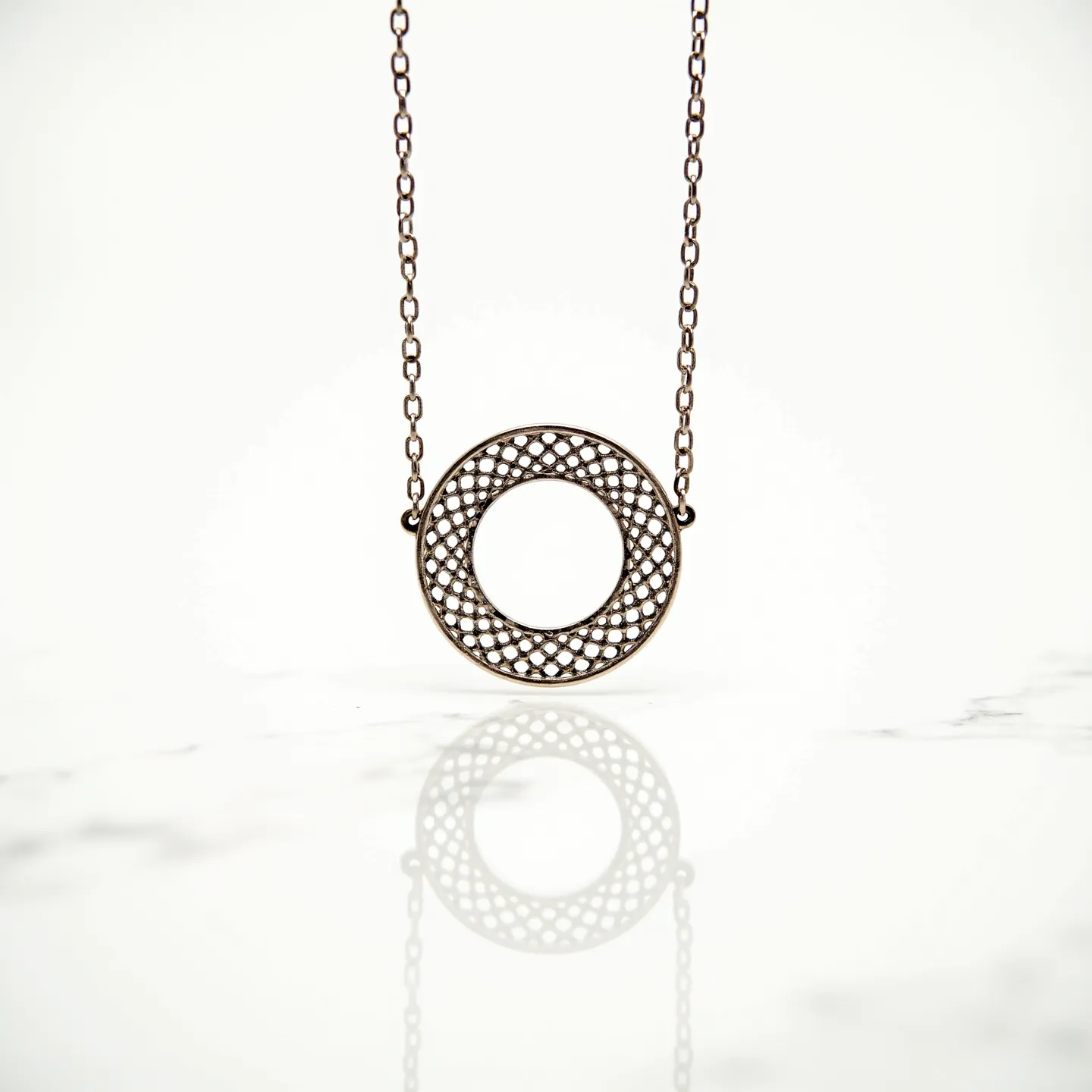 This circle necklace features a delicate and intricate circular pendant composed of a lattice pattern, giving it a detailed and airy appearance. The metal appears to have an antiqued finish, suggesting a choice of materials such as brass or bronze, known for their warm tones and vintage appeal. The pendant is seamlessly connected to a slender chain which complements its style, and the links suggest durability and elegance. While there are no apparent gems or stones set within the pendant, the craftsmanship emphasizes the elaborate design of the latticework. The necklace appears to use a standard clasp mechanism, which not only ensures secure attachment but also maintains the piece's cohesive aesthetic.