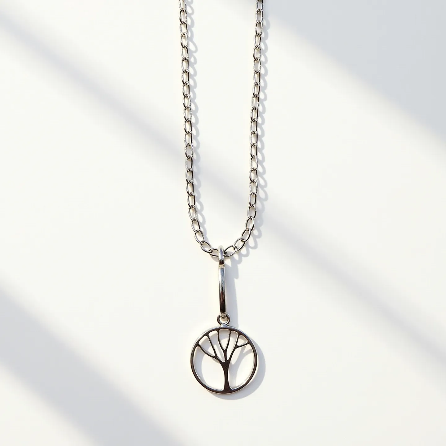 This circle necklace features a sleek, metallic chain with oval links that complement the pendant's design. The pendant is a circular charm crafted in metal, showcasing an artistic tree motif carved out in a minimalist style. The pendant is attached to the chain with a polished metal bail, allowing it to hang freely and move with ease. The clasp, although not visible here, likely offers a secure and seamless connection, adding both style and functionality to the overall piece. The refined simplicity of this necklace makes it versatile and suitable for various occasions.