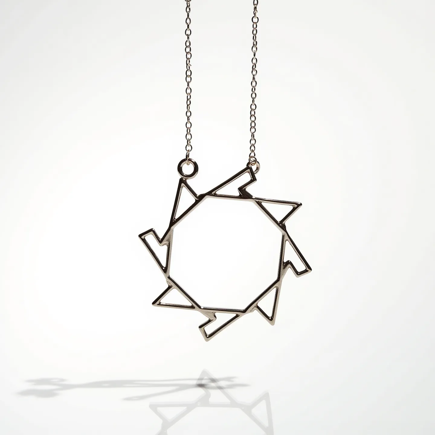 This circle necklace features a geometric pendant crafted from a shiny metal, possibly stainless steel or silver, with a design that incorporates interconnected triangular shapes forming an intricate openwork pattern around a central hexagonal negative space. The pendant is suspended from a delicate chain, likely matching the pendant's material, emphasizing a modern and minimalist aesthetic. The necklace includes small rings attaching the pendant to the chain, ensuring stability and durability. The overall look is contemporary, making it a versatile accessory suitable for various styles and occasions.