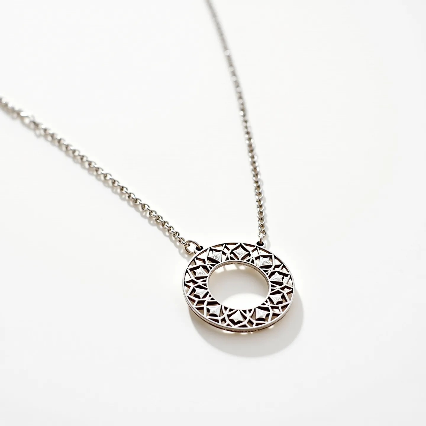 This circle necklace features a polished silver-toned pendant with an intricate geometric pattern, creating an eye-catching open circle design. The pendant is attached to a delicate chain, also in a matching silver tone, which complements the overall aesthetic. The necklace has a simple loop attachment on either side of the pendant, securing it firmly to the chain.