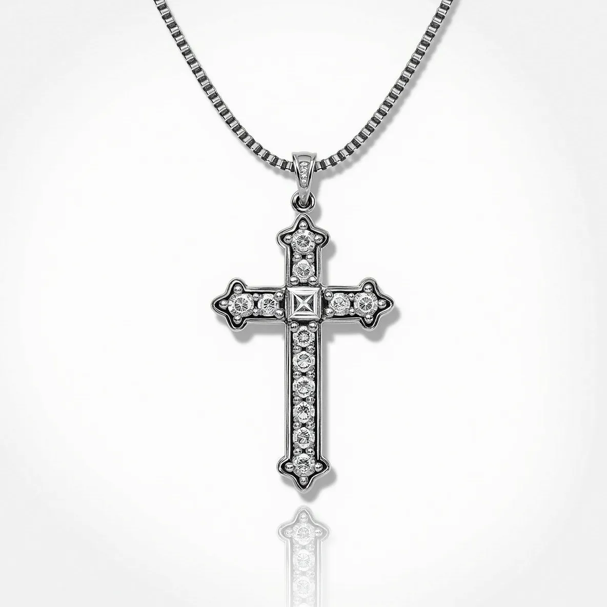 This cross diamond necklace features a cross-shaped pendant adorned with sparkling diamonds. The diamonds, set in a symmetrical pattern, likely include round brilliant and square cuts, with one prominently set in the center. The pendant is crafted from a metal that appears to be white gold or platinum, enhancing the brilliance of the diamonds. The necklace includes a box chain that complements the pendant's elegant style. The connection between the chain and the pendant is secured with a small, unobtrusive bail, contributing to the overall refined appearance of the piece.