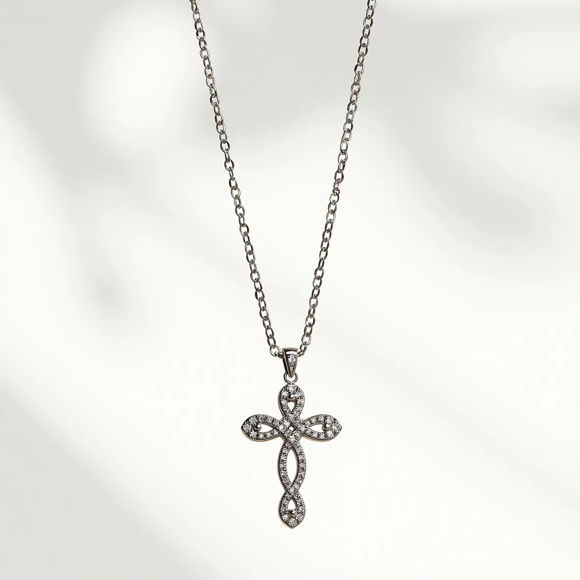 This cross diamond necklace features a beautifully crafted cross pendant adorned with small, round-cut diamonds. The diamonds are elegantly pave-set, offering a sparkling and refined appearance. The cross itself is an ornate design with a gently twisting form, adding a subtle complexity to its shape. It is attached to a slender chain that complements the pendant's design through a secure bail at the top of the cross. The necklace captures a sophisticated yet understated elegance, making it a versatile accessory for both formal and casual attire.