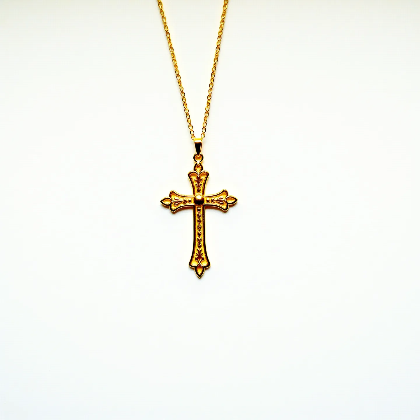 This cross necklace features an intricately designed pendant, crafted from a gold-toned metal that gives it an elegant and polished appearance. The cross showcases decorative embellishments along its length and ends, adding a touch of sophistication. It hangs from a delicate chain, likely made of the same metal, which complements the pendant's ornate details. The attachment appears secure, with a loop at the top of the cross allowing it to connect seamlessly to the chain. The design suggests that it is both a fashionable and symbolic accessory.