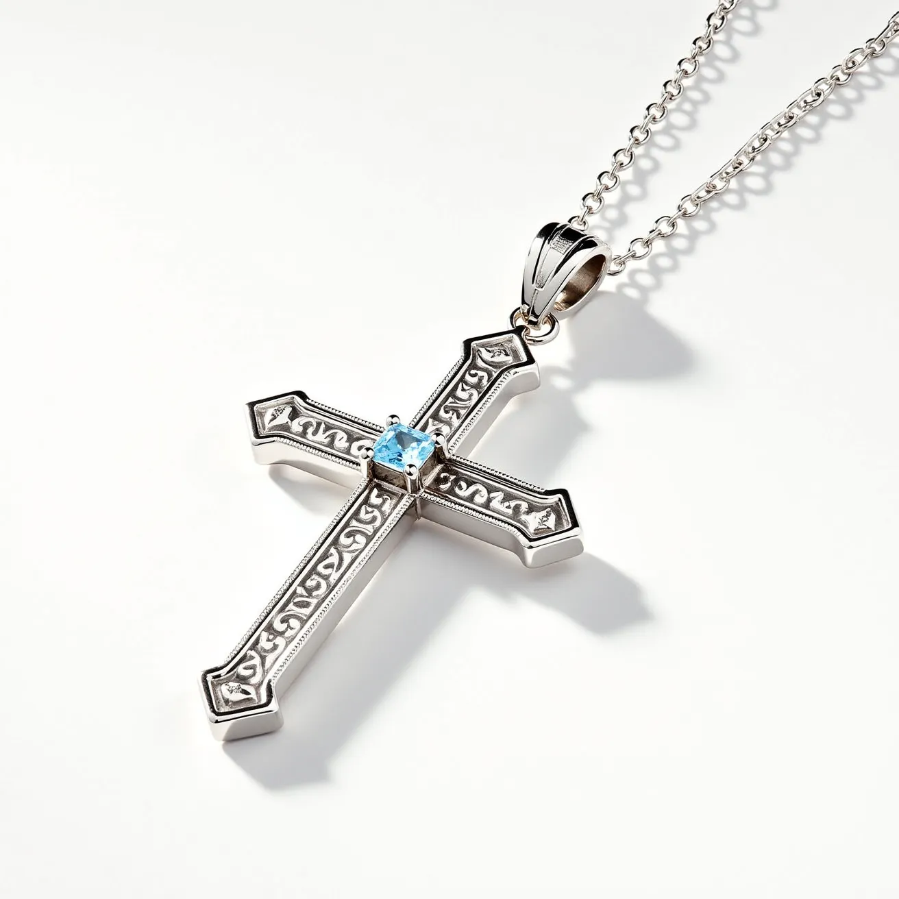 This cross necklace features a sleek silver-toned cross adorned with intricate engraved detailing along its surface. At the center of the cross, a dazzling light blue gemstone, possibly a topaz, is set in a secure four-prong setting, adding an elegant sparkle to the piece. The cross is attached to a delicate chain through a polished silver bail, providing a sturdy yet graceful connection. The overall design combines traditional symbolism with contemporary style, making it a versatile accessory suitable for many occasions.