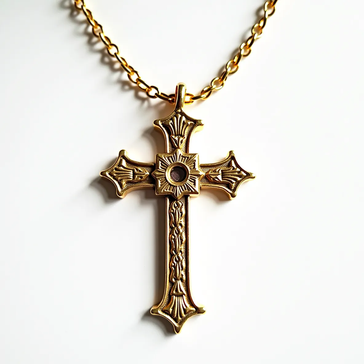 This cross necklace features an ornate design crafted in what appears to be gold-toned metal, exhibiting intricate detailing with floral and textured elements. At the center of the cross, a circular cut setting houses a gem, possibly a small round stone of darker shade, adding a focal point to the piece. The pendant is suspended from a matching gold-toned chain with a standard link pattern, providing secure and elegant attachment. The chain likely includes a clasp for fastening, though specific details of the clasp type are not visible. Overall, the necklace combines traditional religious symbolism with decorative artistry.