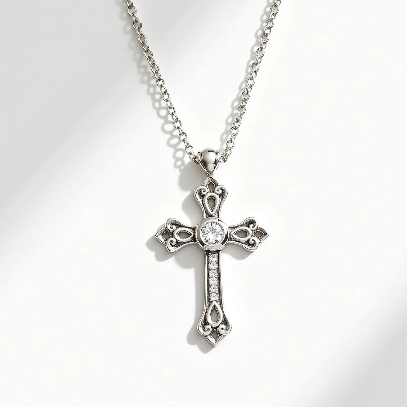 This cross necklace features a detailed design with an elegant silver material that captures a classic aesthetic. The cross is adorned with a round-cut gem prominently set in the center, surrounded by intricate metalwork that enhances its elegance. Along the vertical beam of the cross, smaller round gems are embedded in a linear setting. The pendant hangs from a delicate chain with a robust attachment, ensuring secure wear.