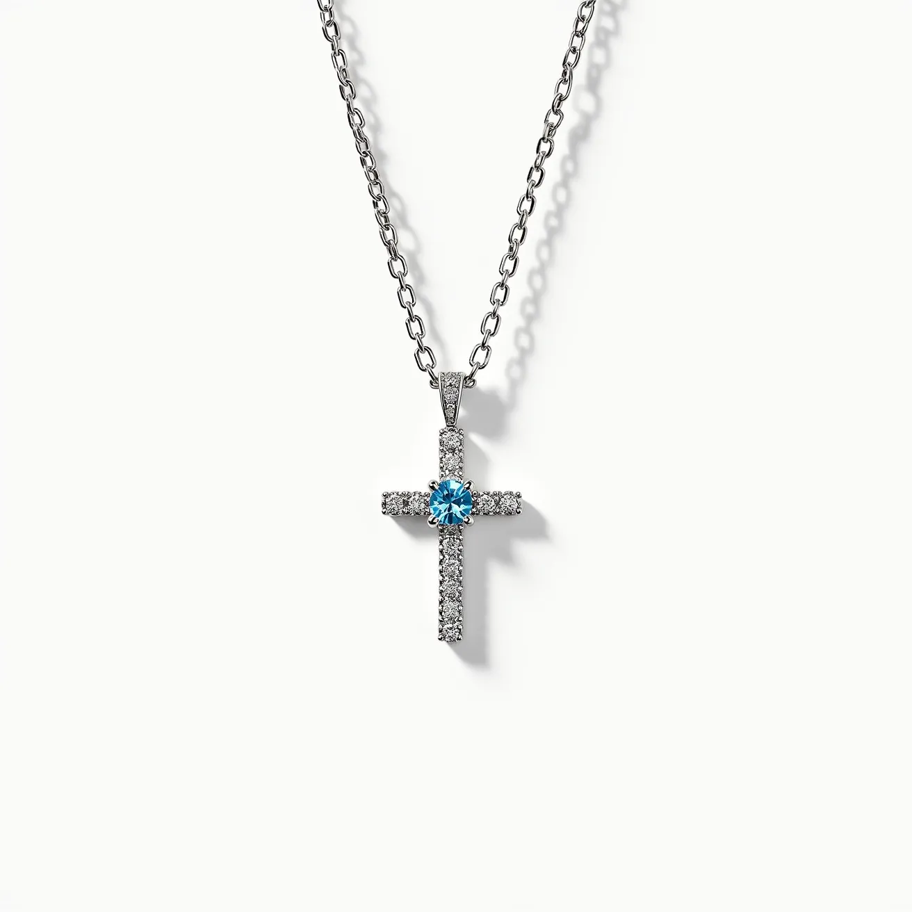 This cross necklace features a delicate chain that appears to be crafted from a silver-colored metal, offering a sleek and polished appearance. The pendant is in the shape of a cross and is adorned with small, clear stones, likely diamonds or cubic zirconia, throughout its length, each set in a pavé setting that enhances their sparkle. At the center of the cross is a larger, round-cut blue gemstone, possibly a blue topaz or sapphire, securely held in a prong setting to showcase its brilliance. The necklace is completed with a simple, elegant clasp that complements the overall design, ensuring both style and functionality.