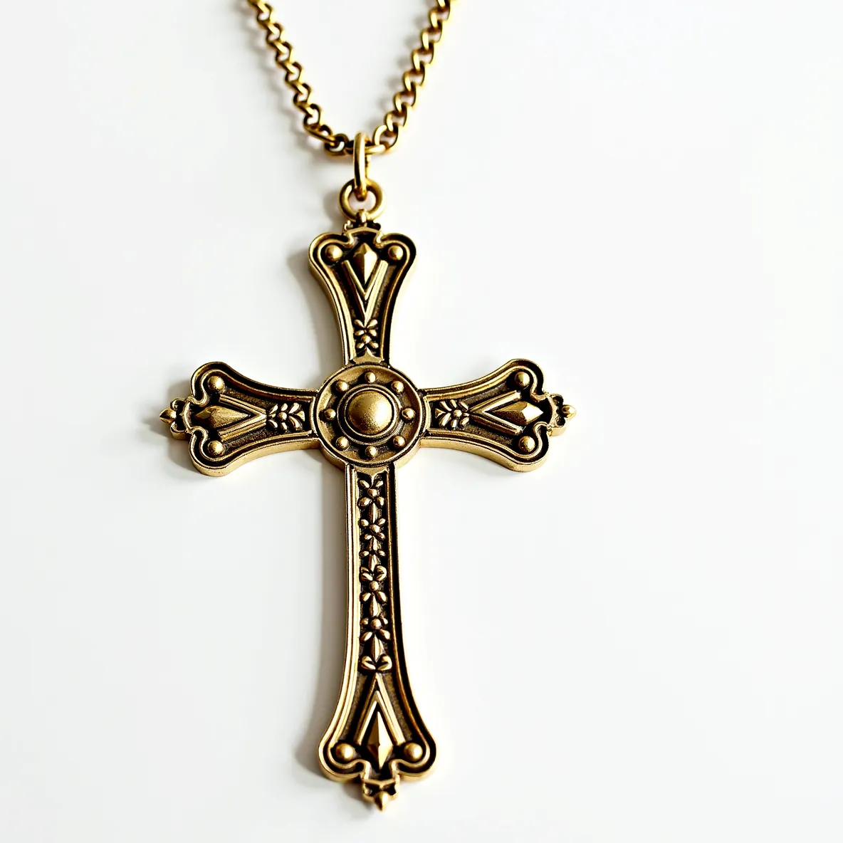 This cross necklace features an ornate design crafted from a gold-toned metal, displaying intricate detailing along its surface. The cross is embellished with a central circular accent that appears studded with a raised, dome-like feature, lending a focal point to the design. Each arm of the cross showcases floral and geometric patterns, creating a sense of symmetry and elegance. The piece is suspended from a matching gold-toned chain with a series of interlinked oval links, and it attaches to the cross via a simple ring bail, ensuring secure and durable wear. The overall aesthetic combines elements of classical and ornate motifs, making it a striking accessory.