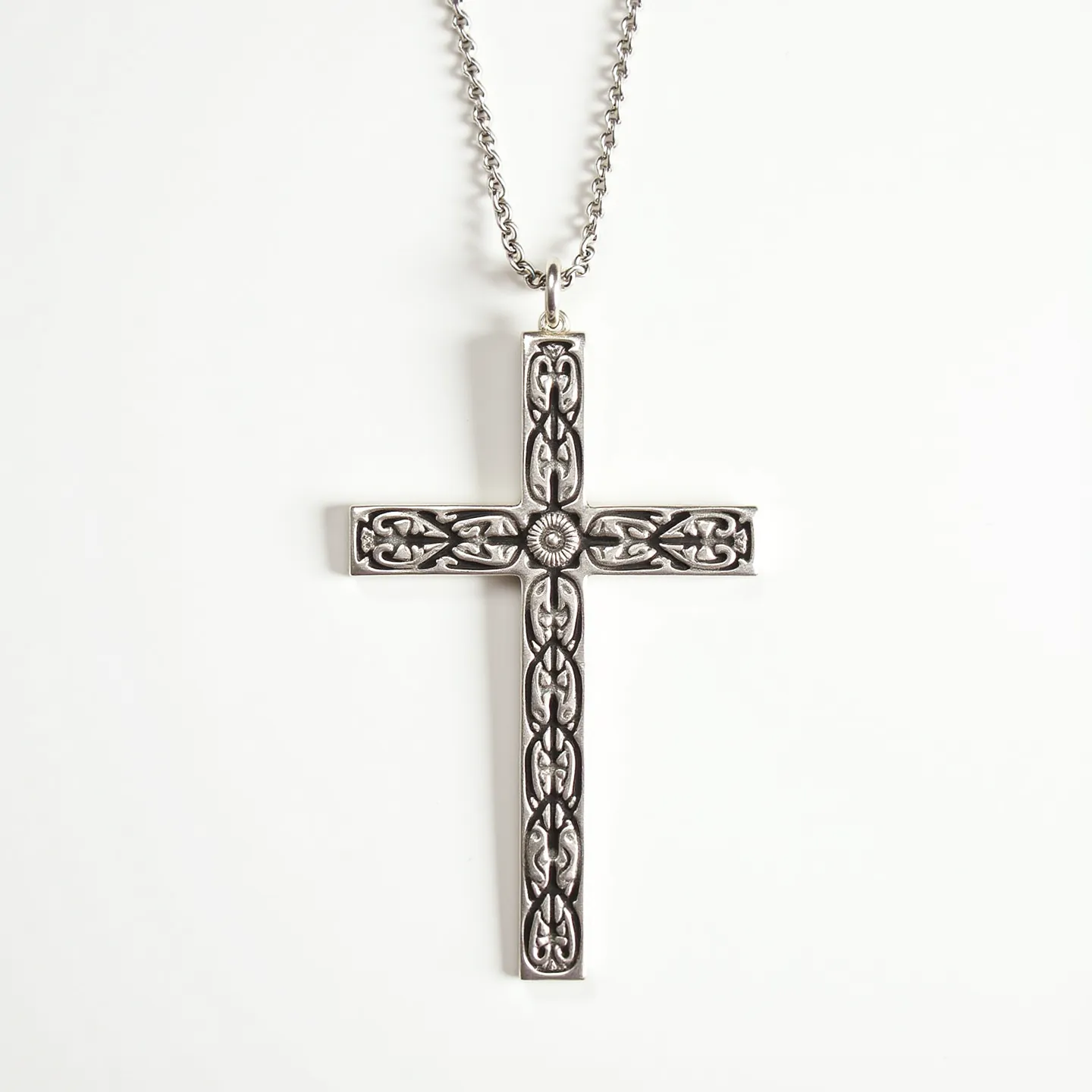 This cross necklace features a beautifully crafted design made of silver-toned metal, with an intricate pattern along the surface that resembles an ornate, filigree motif. The design is highlighted by a central, circular embellishment that adds to its intricacy. The cross pendant is suspended from a matching chain that is likely composed of the same metal, ensuring a cohesive appearance. The attachment consists of a small, unobtrusive bail that connects the pendant to the chain, allowing it to hang elegantly. The chain appears to utilize a simple clasp, likely a lobster clasp, which provides a secure closure while maintaining the necklace's overall aesthetic.