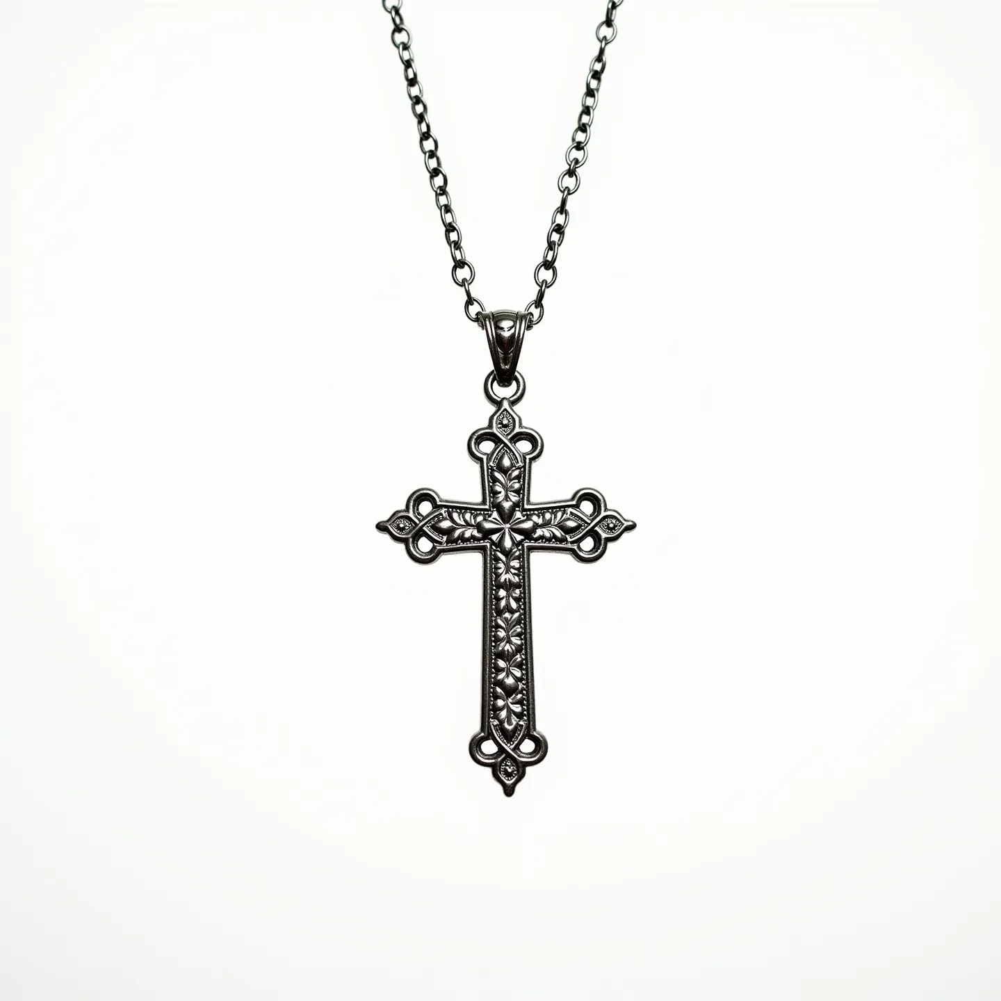 This cross necklace features an intricately designed pendant crafted from a metallic material, possibly silver or stainless steel, which gives it a sleek and polished appearance. The cross is adorned with an ornate pattern that resembles floral or vine motifs, adding a touch of elegance and intricate detail to the piece. The overall design is gothic-inspired, with decorative tips on each arm of the cross. It is suspended from a matching chain that appears to be a standard cable link, providing both durability and style. The pendant is secured to the chain with a classic bail, ensuring it hangs securely and gracefully.