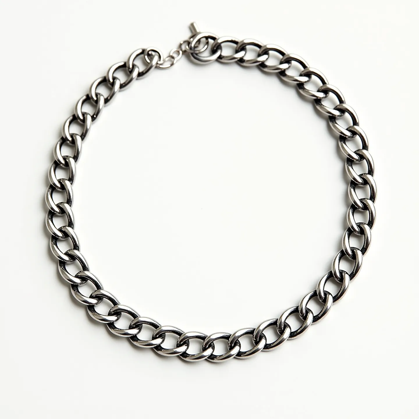 This curb chain is crafted from a polished metal, likely stainless steel, which gives it a sleek and shiny appearance. The links are thick and uniform, lying flat in a traditional curb style, known for its durability and classic look. The chain is secured with a simple toggle clasp, which adds to its streamlined design and ease of use. There are no gemstones or additional embellishments, emphasizing its minimalist yet bold aesthetic.