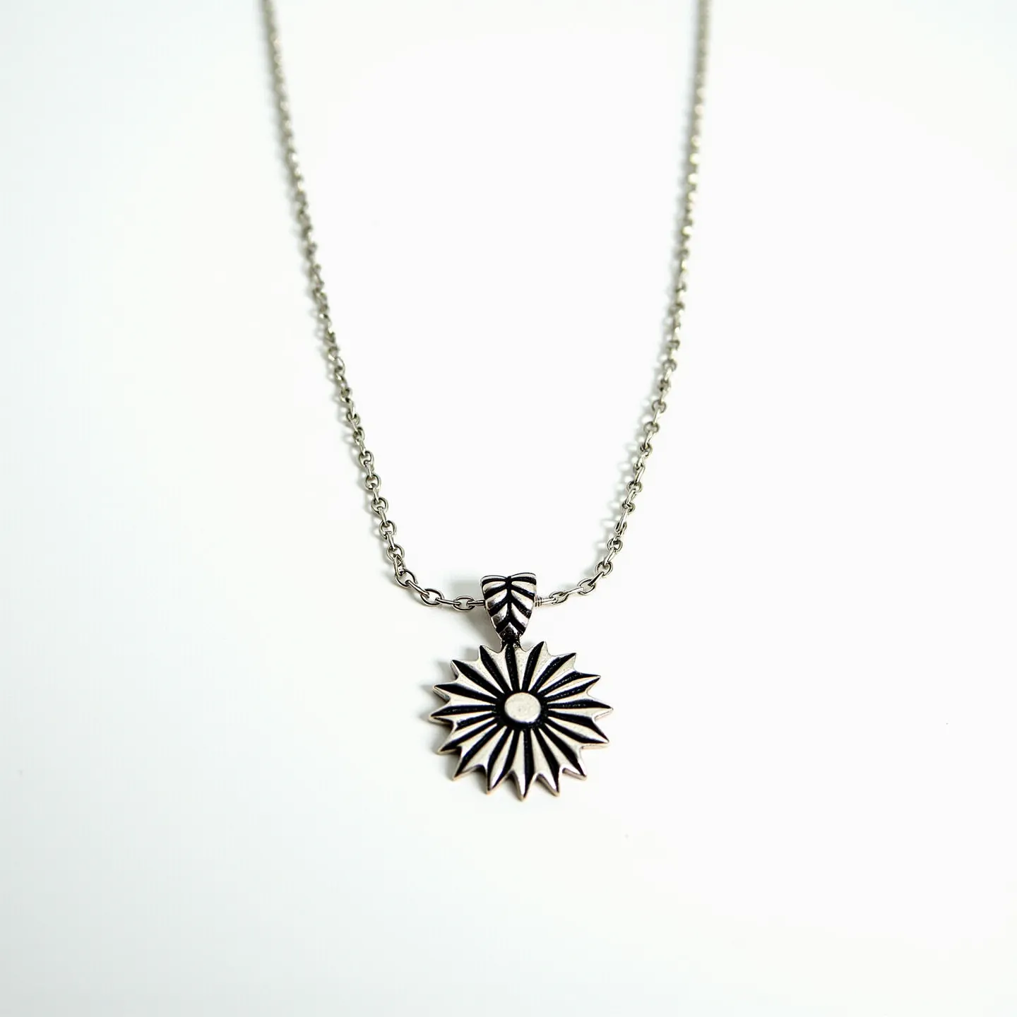 This custom charm necklace features a delicate chain crafted from metal that appears silver in color. The focal point of the necklace is a beautifully designed charm resembling a stylized flower or starburst, made from the same metallic material as the chain. The charm is attached to the chain via a decorative bail that features an engraved or textured pattern, adding an intricate detail to the piece. The necklace likely uses a standard clasp mechanism like a lobster clasp, which is commonly used for such designs. The overall aesthetic of the necklace is elegant and contemporary, suitable for various occasions.