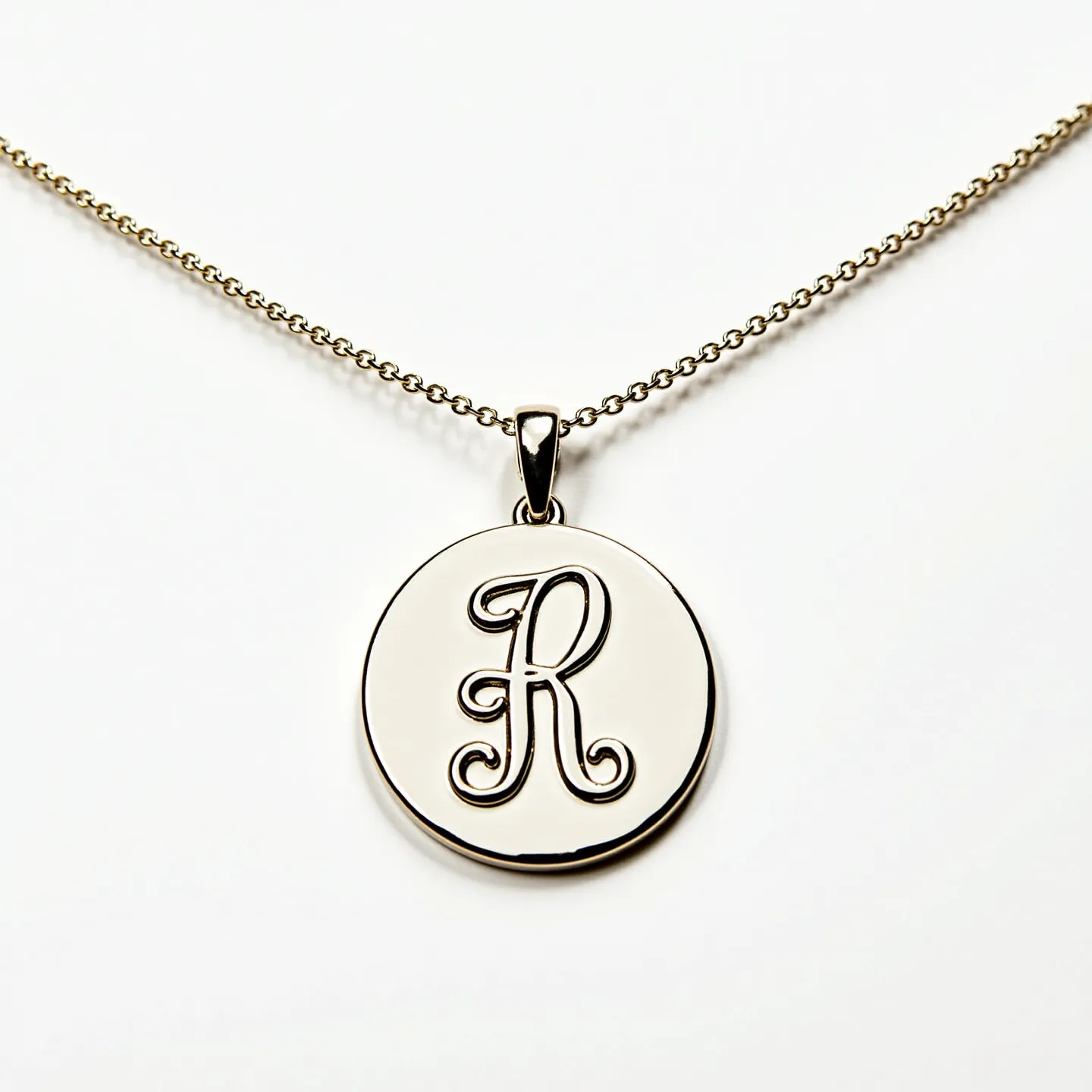 This custom charm necklace features a polished, circular pendant engraved with a decorative letter "R" in the center. The pendant is likely made from a metallic material, giving it a sleek, shiny finish. It is suspended from a delicate link chain that complements the pendant's simple elegance. The chain is attached to the pendant with a secure bail, ensuring it hangs gracefully around the neck. The necklace does not appear to include any additional gems or stones, focusing instead on the personalized charm of the engraved initial.