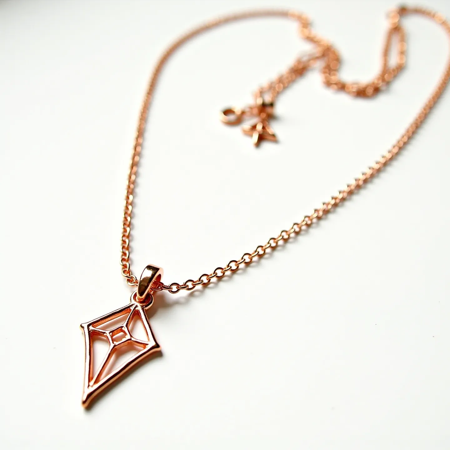 This custom charm necklace features a sleek chain crafted from polished rose gold metal, exhibiting a warm, metallic sheen. The necklace showcases a kite-shaped pendant with an openwork design, exuding a modern and minimalist aesthetic. The pendant is securely attached to the chain via a fixed bail, allowing it to lay flat when worn. The design is complemented by a classic lobster clasp, providing a secure and adjustable closure. This thoughtfully designed piece combines elegance with a touch of contemporary flair, making it a versatile addition to any jewelry collection.