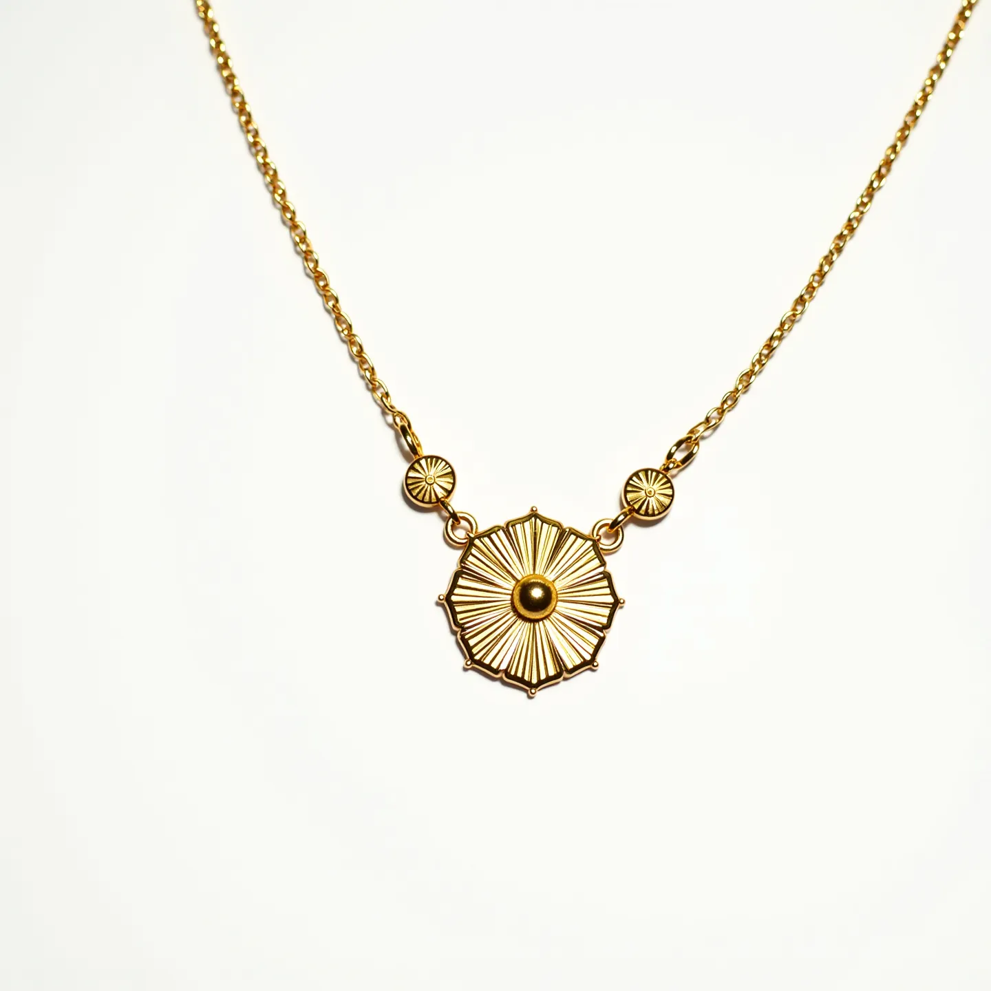 This custom necklace features a gold-toned chain with a striking central pendant design. The pendant showcases intricate radial patterns reminiscent of a sunburst, crafted from the same gold-toned metal, and accented by a central raised dot. Flanking the main pendant, smaller circular designs echo the sunburst theme, adding symmetry and balance. The attachment is an elegant cable chain, enhancing the necklace's classic yet contemporary aesthetic. The necklace likely employs a standard clasp, completing its refined look and allowing for secure wear.