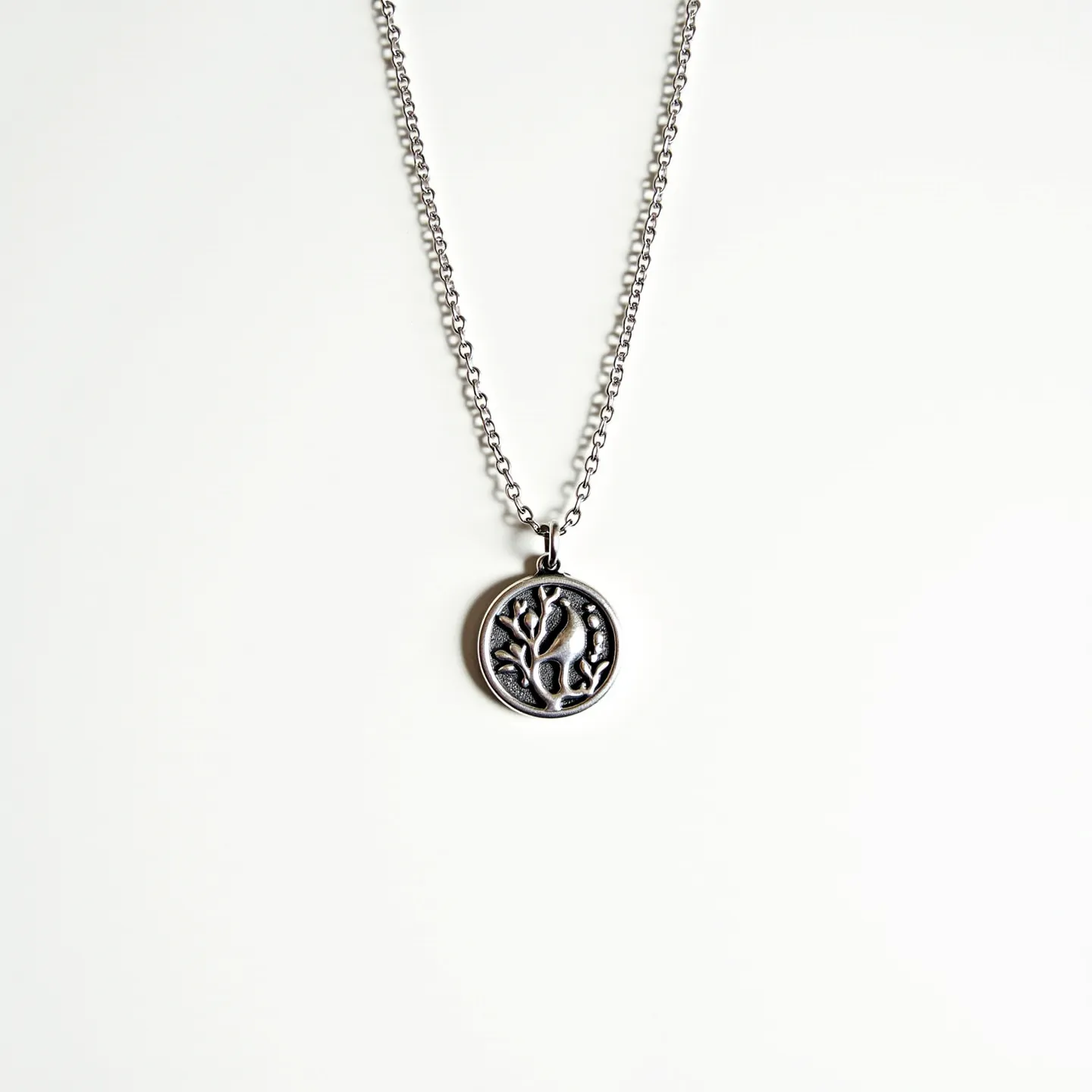 This custom necklace features a finely crafted metal chain and a circular pendant with an intricate raised design resembling a tree. The pendant is attached to the chain through a small loop at the top. The chain appears to be made of a metal such as silver or stainless steel, characterized by a smooth finish and a uniform link pattern. The pendant itself displays a dark patina within the recessed areas, enhancing the contrast and detail of the design. The necklace likely fastens with a standard clasp, typical of such chain designs, ensuring a secure fit when worn.